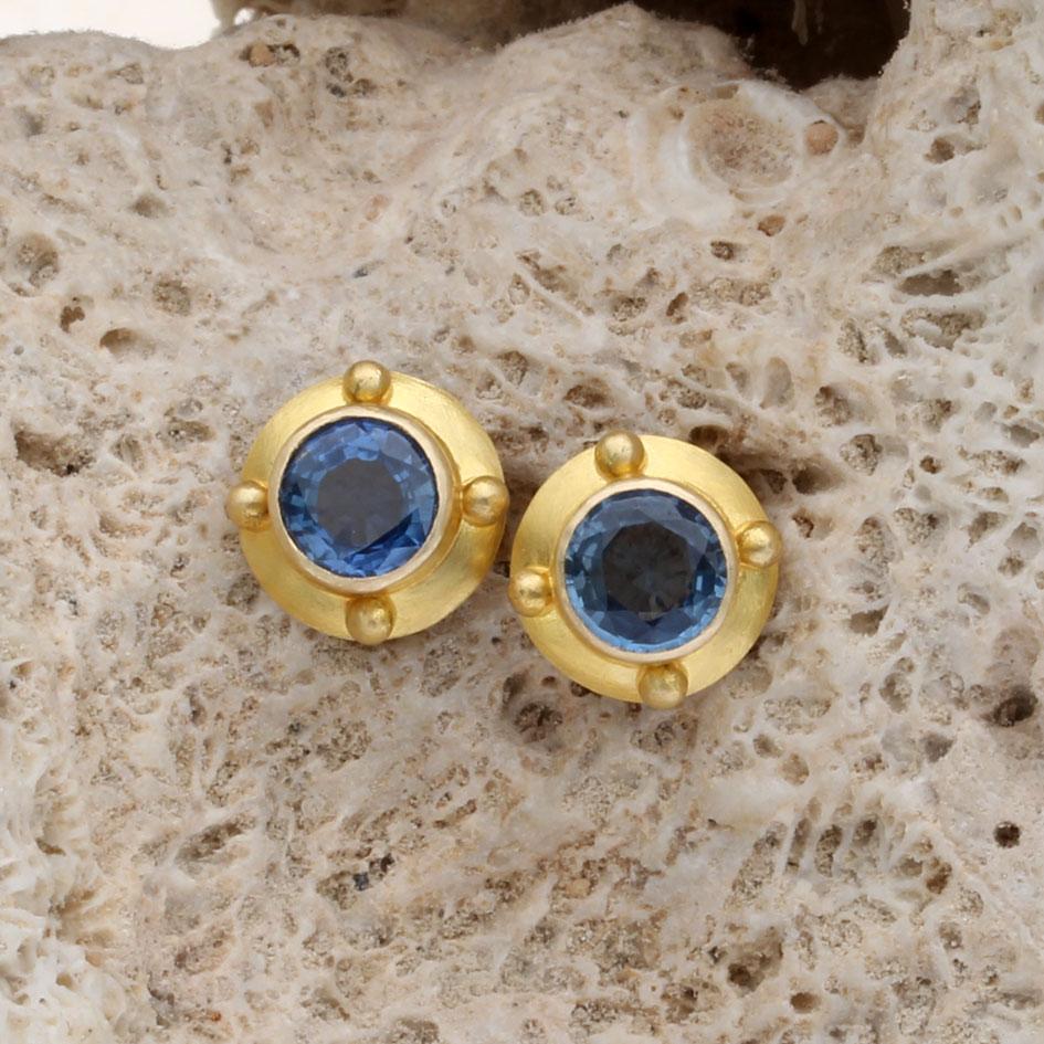 Deux saphirs bleus ronds de 5 mm à facettes sont sertis dans de larges doubles chatons arrondis en or 18K mat avec quatre grandes granulations 