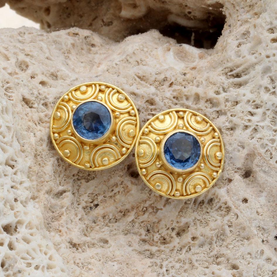 Due luminosi zaffiri blu sfaccettati di 5 mm sono incastonati in castoni d'oro 18 carati finemente lavorati su uno sfondo d'oro leggermente bombato e decorato con ornamenti in granulato 