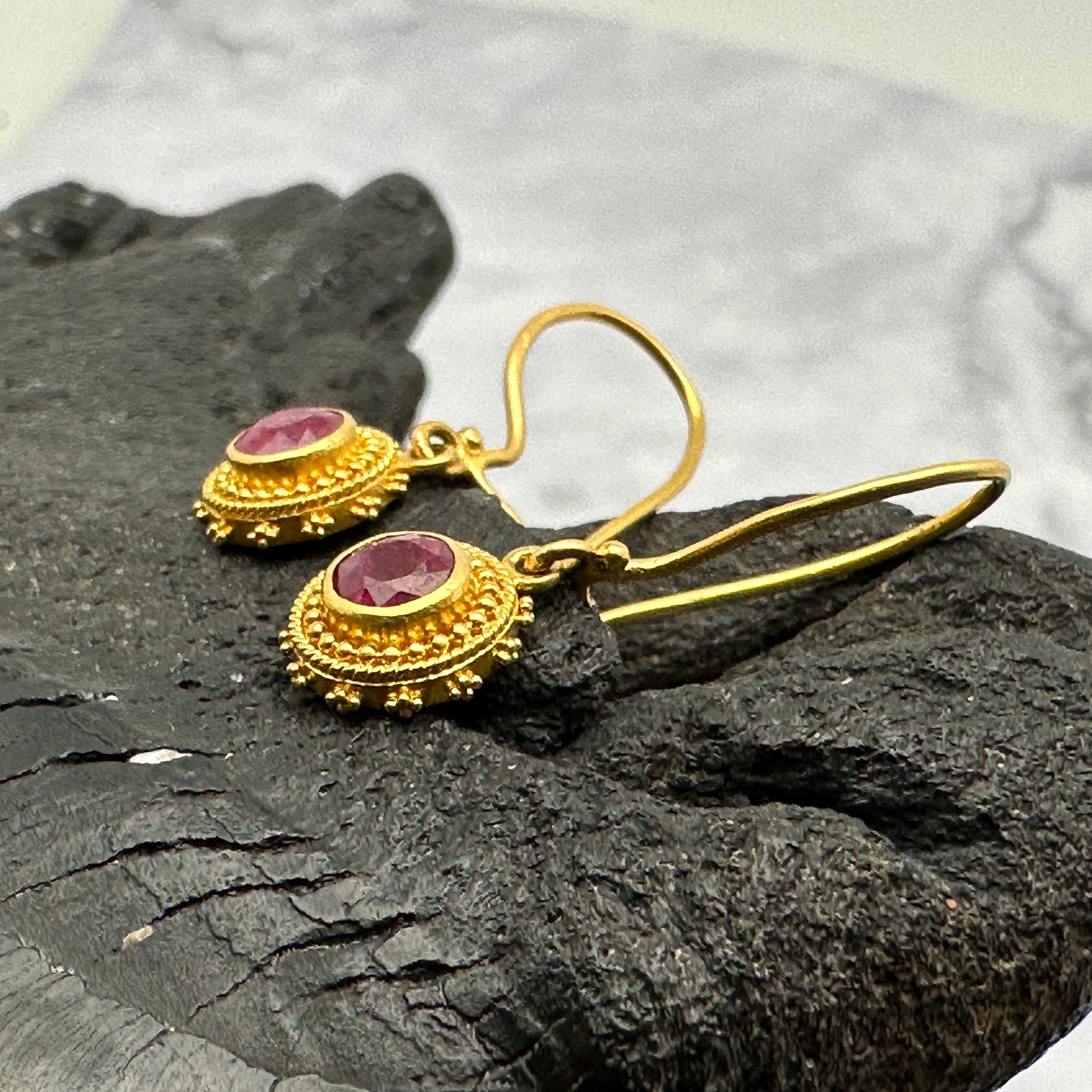 Two 4 mm round faceted rubies are set in a cylindrical radiating granulated high Karat setting in this exquisite example of artisanal gold-smithing art.  Beautiful color to dangle below safety clasp wires.  Nice!
