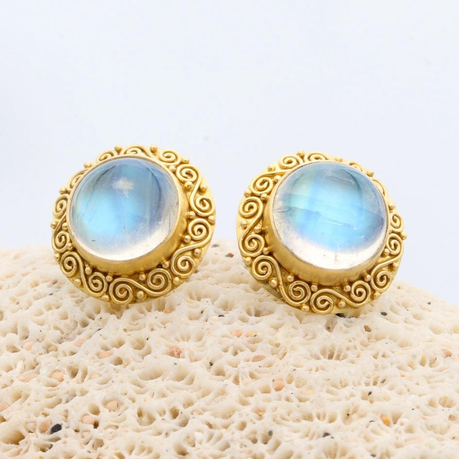 Two luminous and blue-shimmering 10 mm round rainbow moonstones are surrounded by artisan crafted 