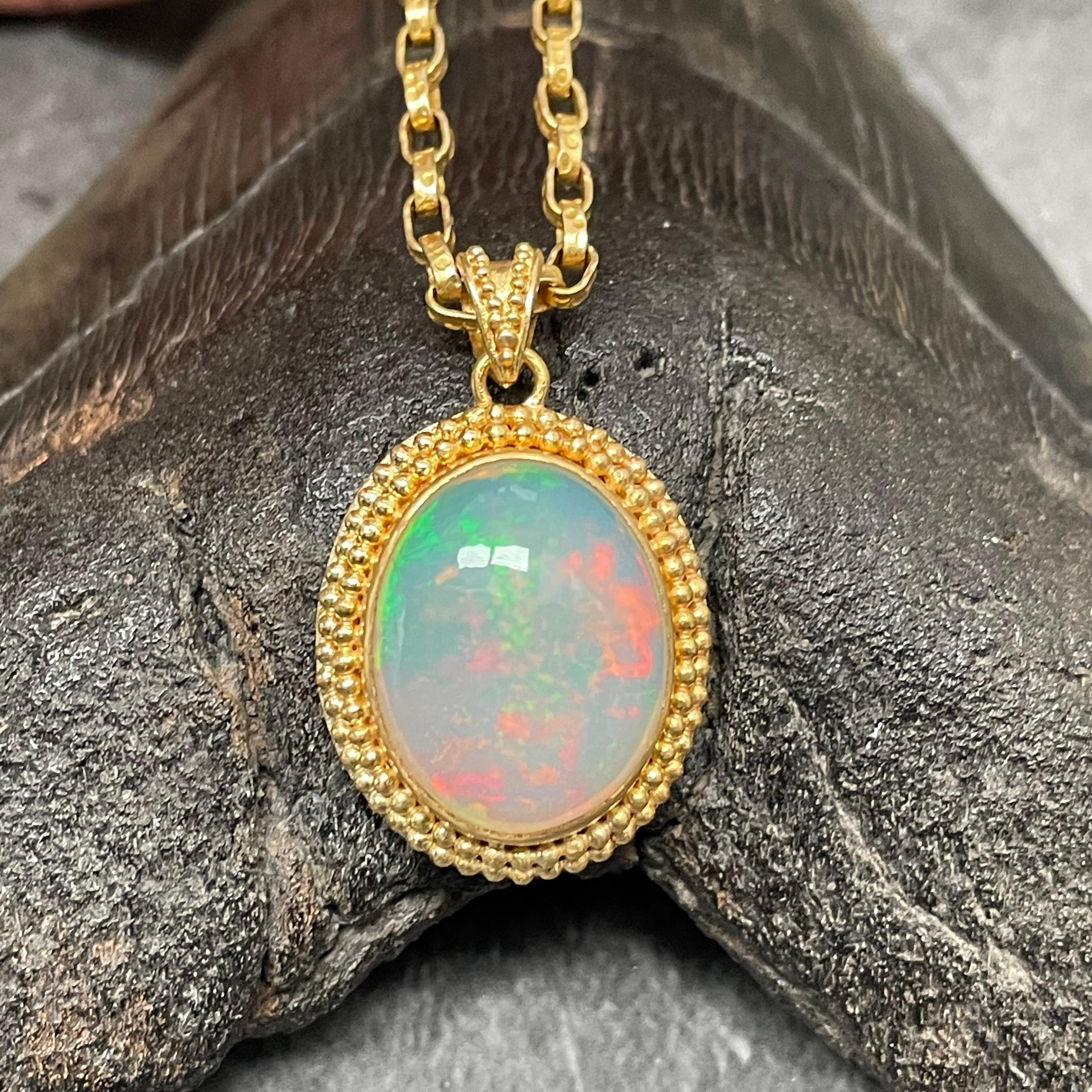 A flashing oval 15 x 18 mm cabochon of high grade Ethiopian Welo opal is surrounded by double stacked rows of 22K granulation with a similarly ornamented bail in this classic handmade creation.  Shades of green, red and yellow.   This piece is