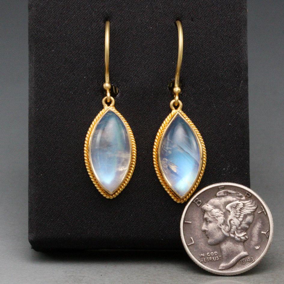 Two 8 x 16 mm marquis shaped rainbow moonstone cabochons are held in simple twist wire accented 18K gold bezels beneath safely clasp wires in this elegant design.  The luminous and ever-changing flashing blue contrasting with the rich color of the