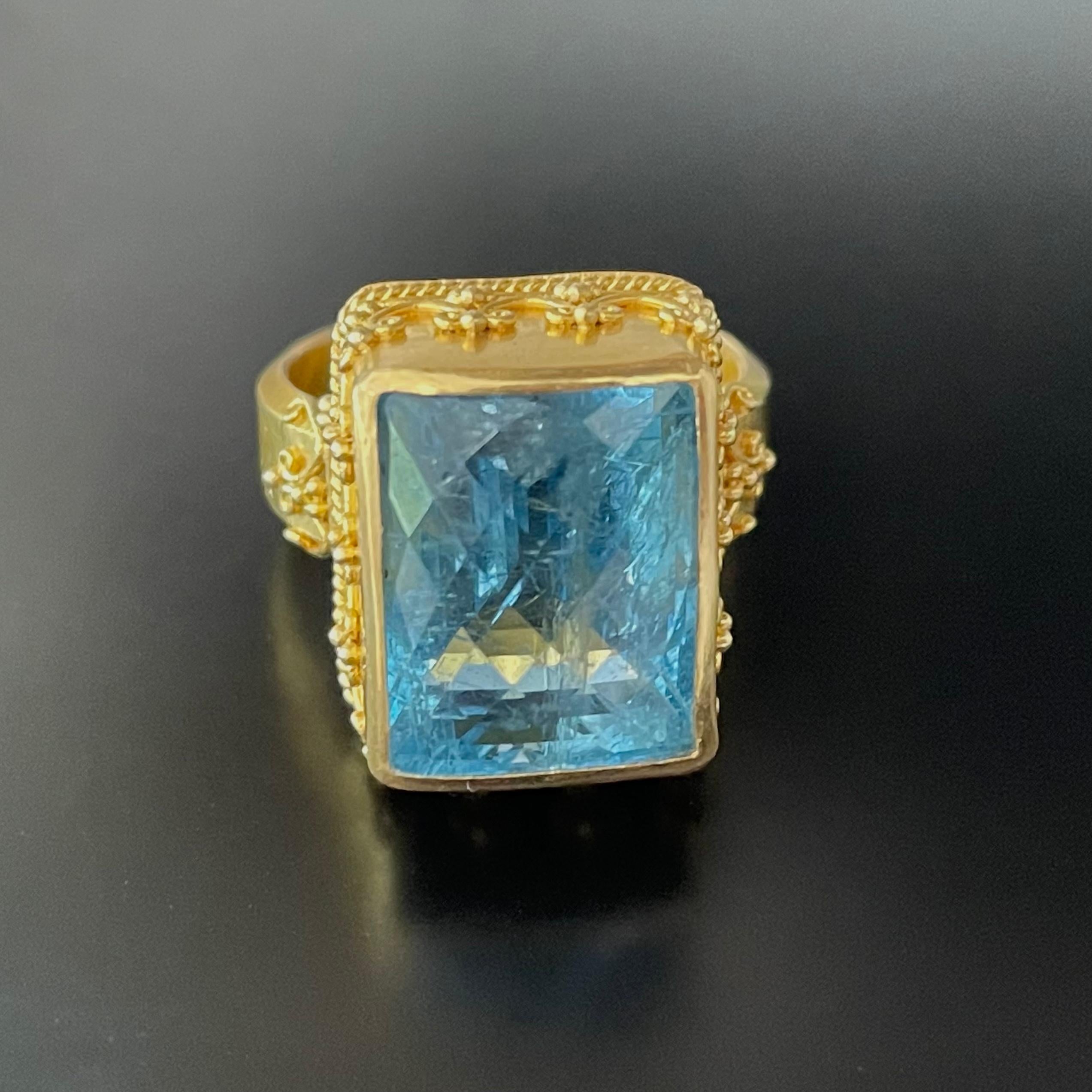 A lively deep blue diagonal checkerboard cut 10 x 13 mm Brazilian Aquamarine is set in this finely decorated handmade 22K design from Steven Battelle.  All the wire and granulation detail was carefully applied over 3 days of work by a master