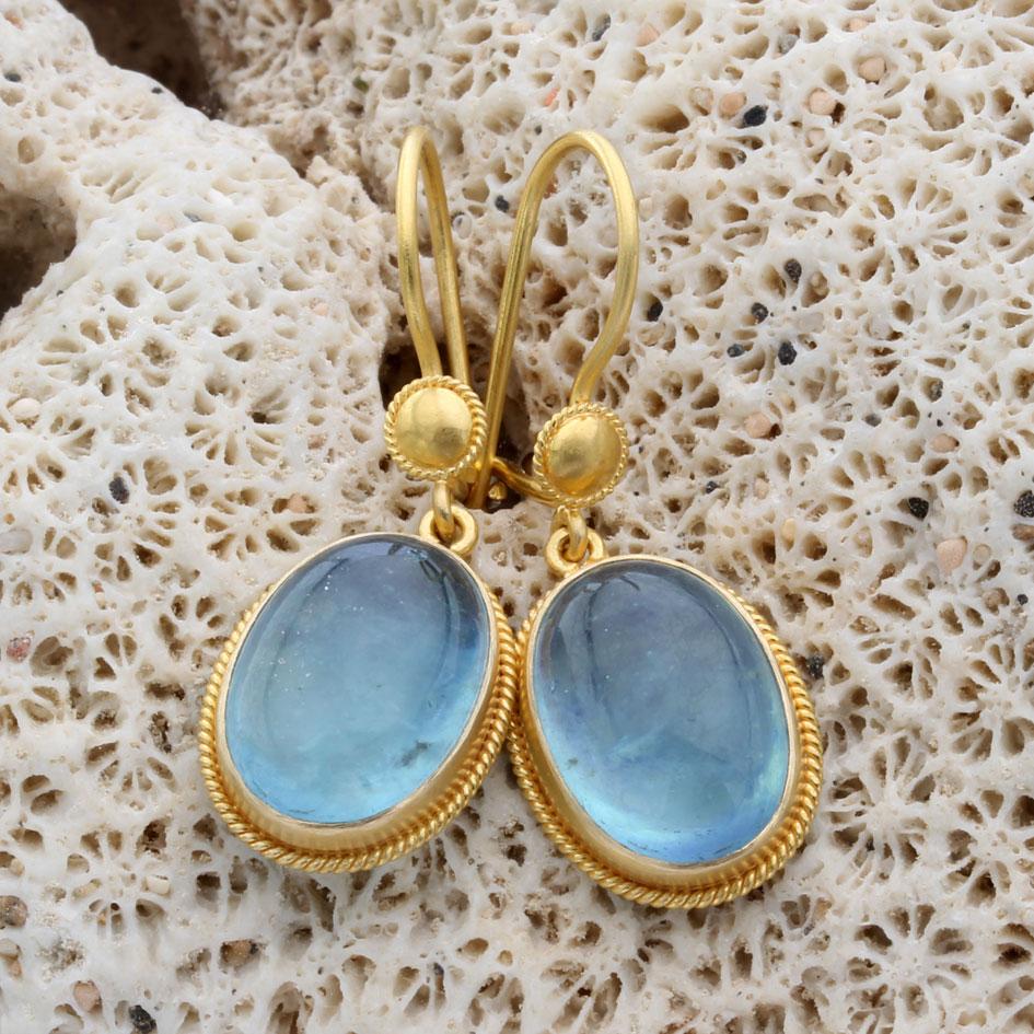 Two limpid blue 10 x 14 mm oval cabochon aquamarines are held in delicate 