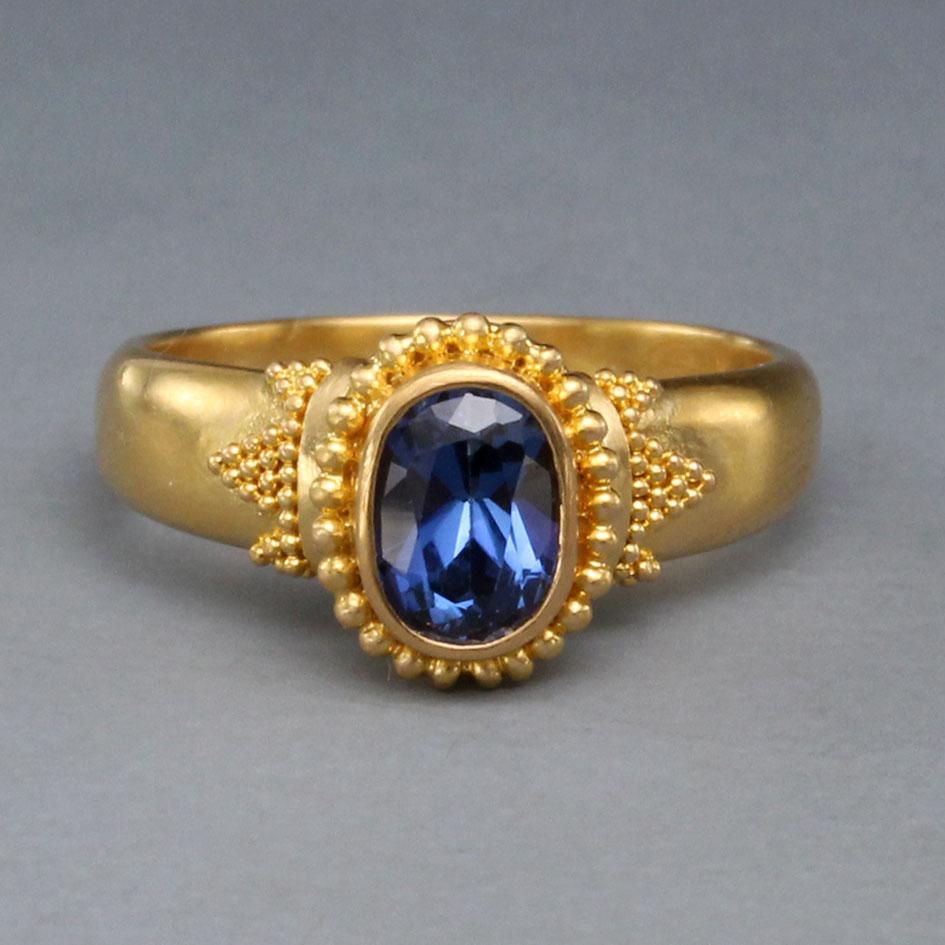 A brilliant blue, high grade 5 x 7 mm oval faceted Thailand blue sapphire is set in a beautifully handcrafted high-karat 22K gold setting with both large and small 
