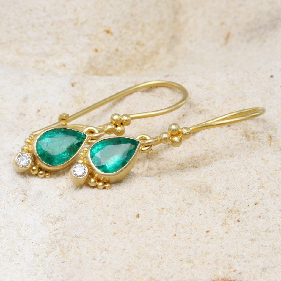 Two crystalline high-grade 4 x 6 mm pear shaped faceted emeralds are set in simple matte-finish 18K gold bezels with 1.8 mm VS1 diamonds centered between graduated sized 18K granulation at the bottom. The safety clasp wires in this ancient-inspired