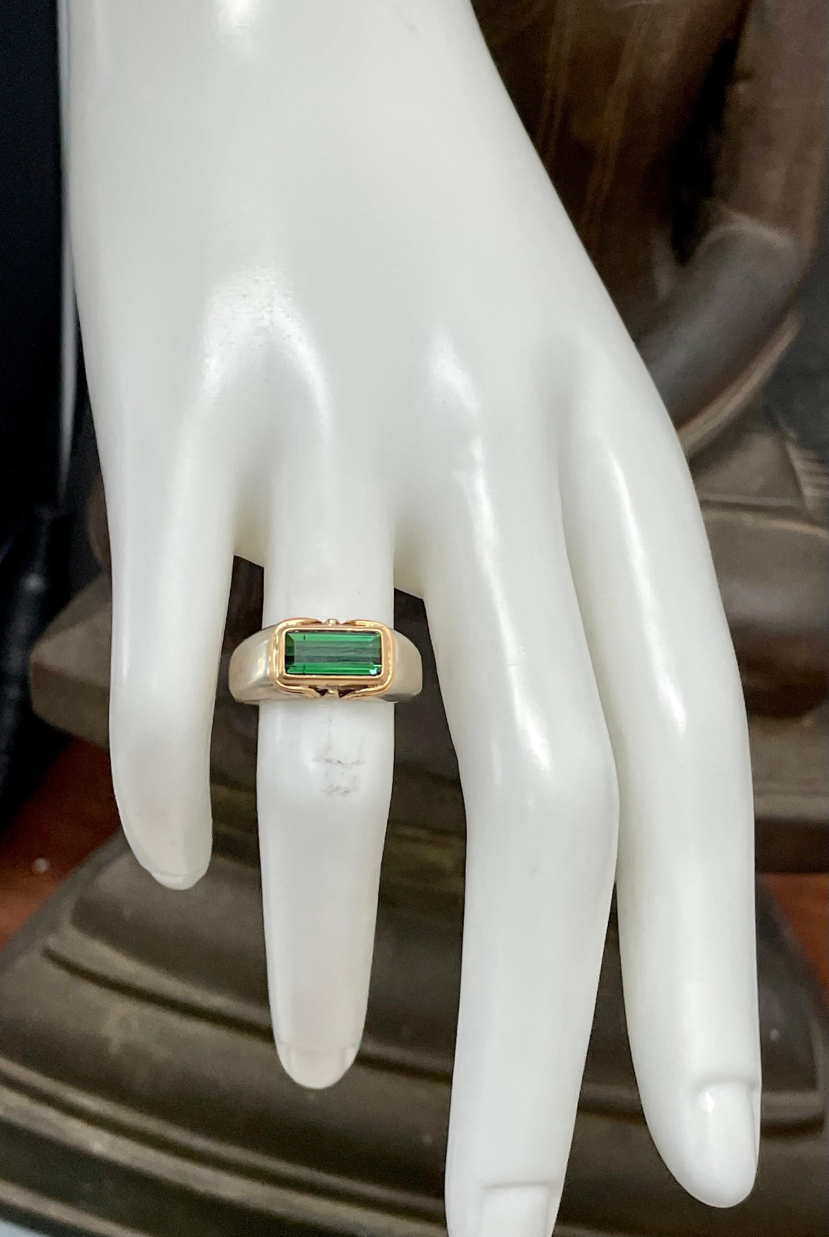Une tourmaline verte rectangulaire à facettes de 5 x 10 mm repose horizontalement dans un chaton en or jaune 18 carats entouré de deux fils d'or jaune 18 carats au sommet d'une tige complémentaire légèrement effilée en or blanc 14 carats.  Cette