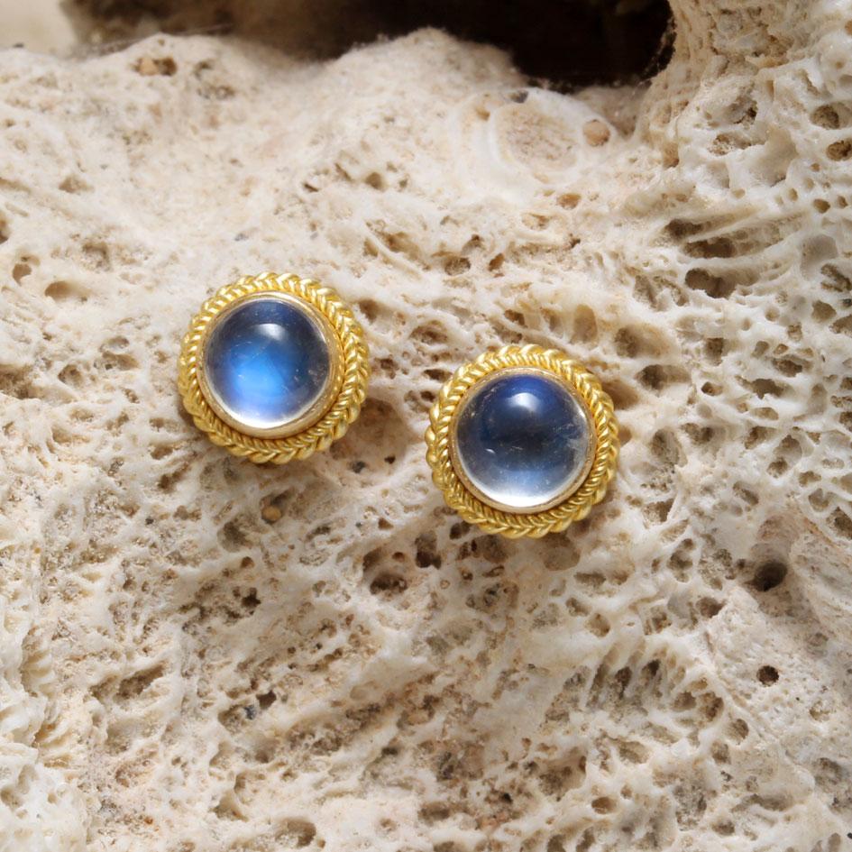 Due cabochon di pietra di luna arcobaleno blu e luminosi da 5 mm sono circondati da lussuosi castoni in oro 18 carati 