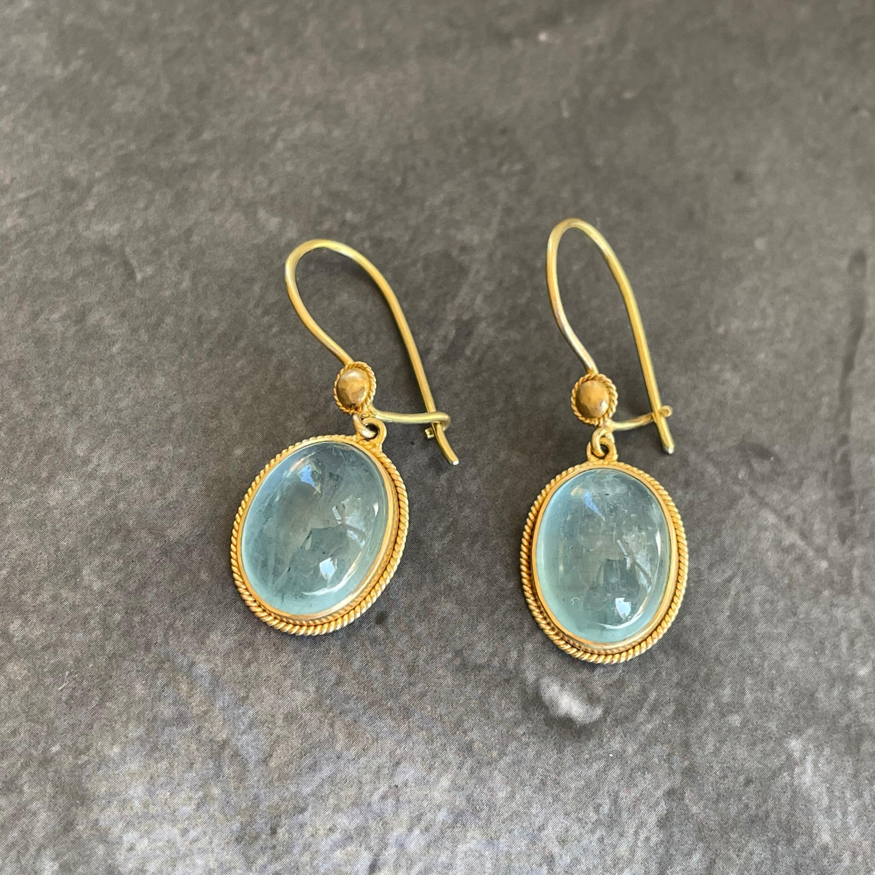 Two limpid oval 10 x 13 mm aquamarine cabochons  are surrounded by elegant twist wire accented bezels and suspended from similar small ear wire accents in this simple but luxurious design from Steven Battelle.  Safety clasp ear wires to prevent