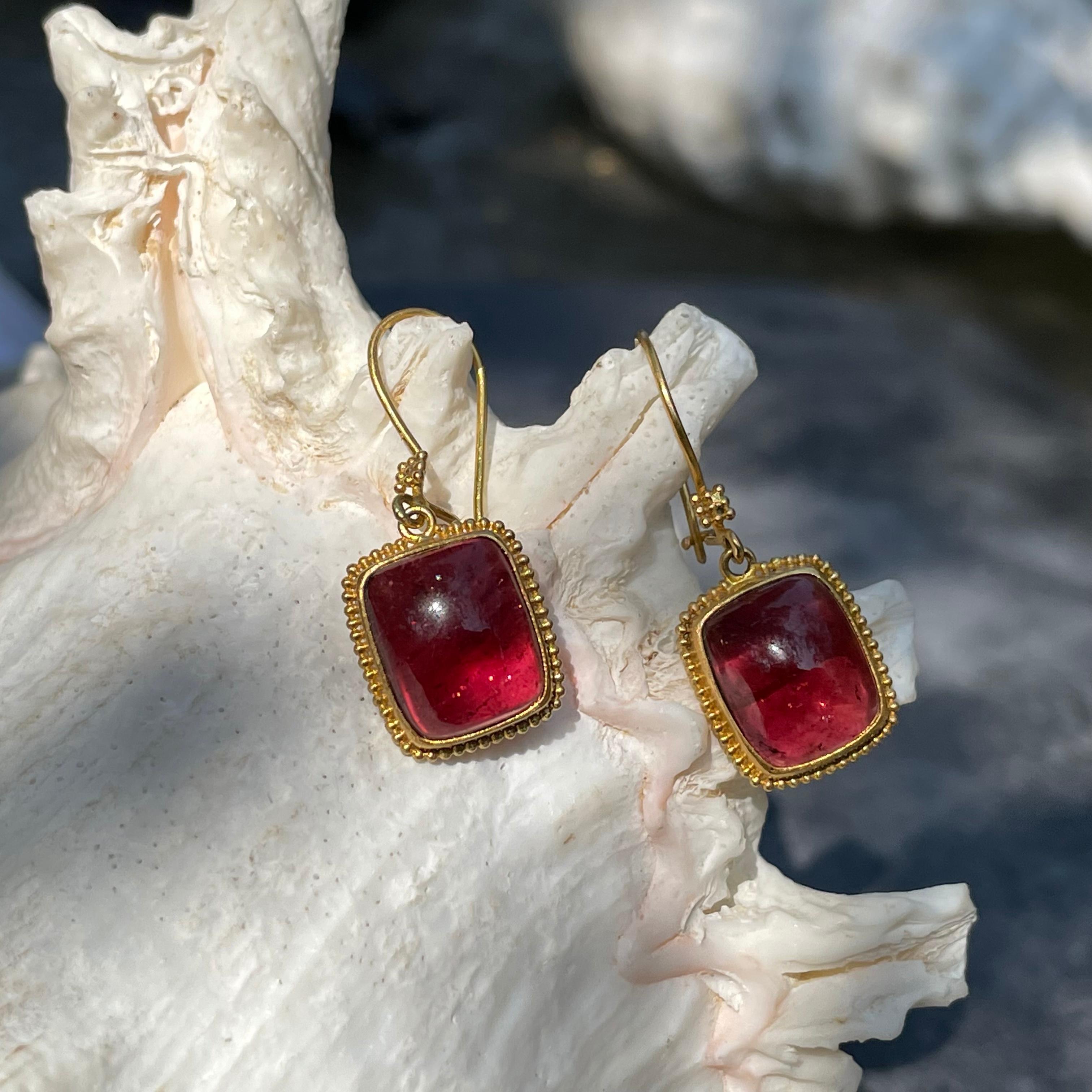 Two matching 10 x12 mm cushion cabochons of Mozambique pink tourmaline are accented by delicate hand applied granulation and suspended below tiny granulated squares in this Steven Battelle high carat gold design. 18K Safety clasp wire closures for