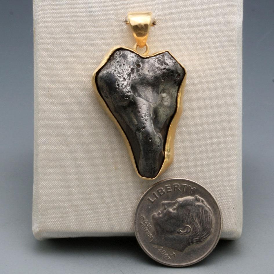 A somewhat irregular 18 x 26mm heart shaped fragment of Sinkote-Alin meteorite with a fusion crust from its flaming entry through the atmosphere is set in simple matte-finish 18K gold bezel  A large iron meteorite fell on the Sikhote-Alin Mountains,