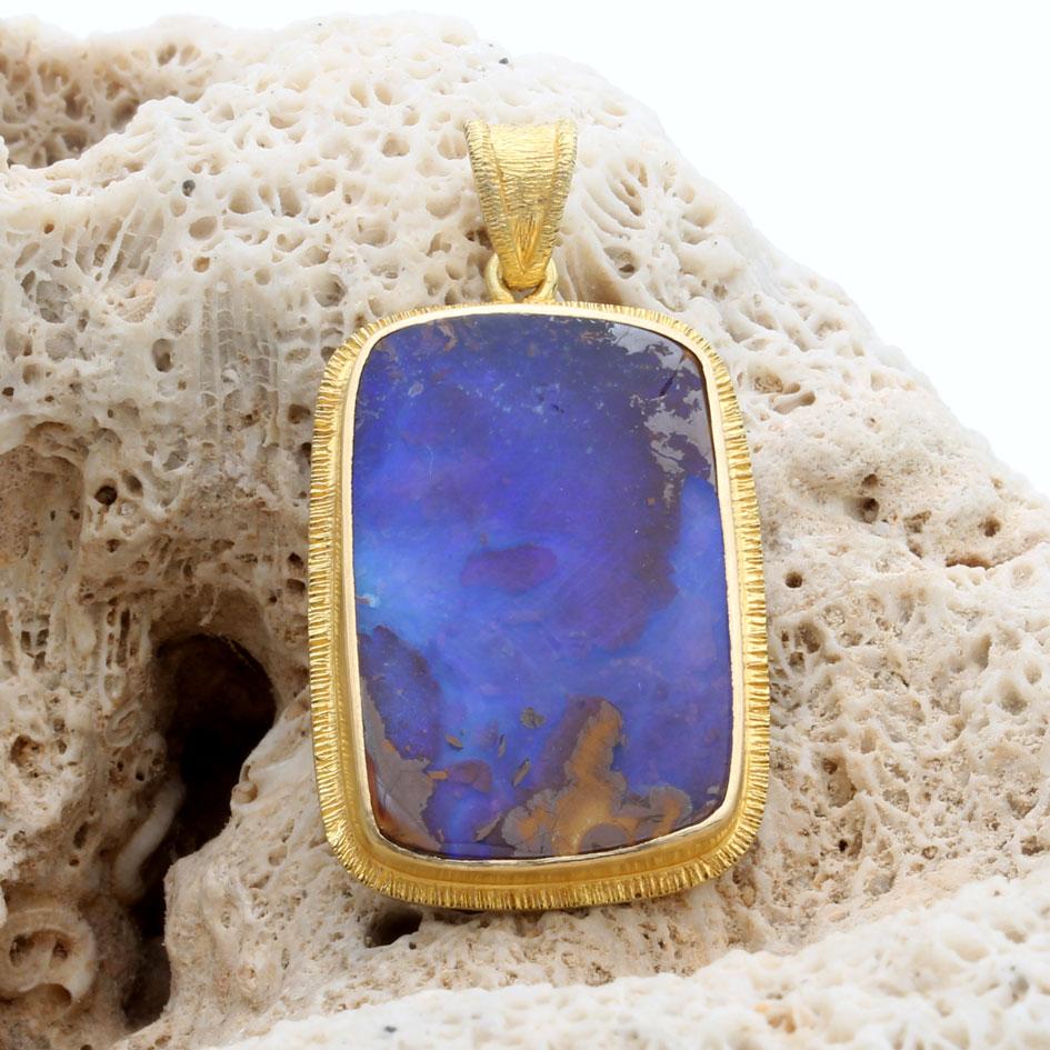Un cabochon semi-rettangolare di opale australiano Quilpie boulder di colore blu intenso 16 x 24 mm è montato in un'incastonatura artigianale in oro 18 carati 