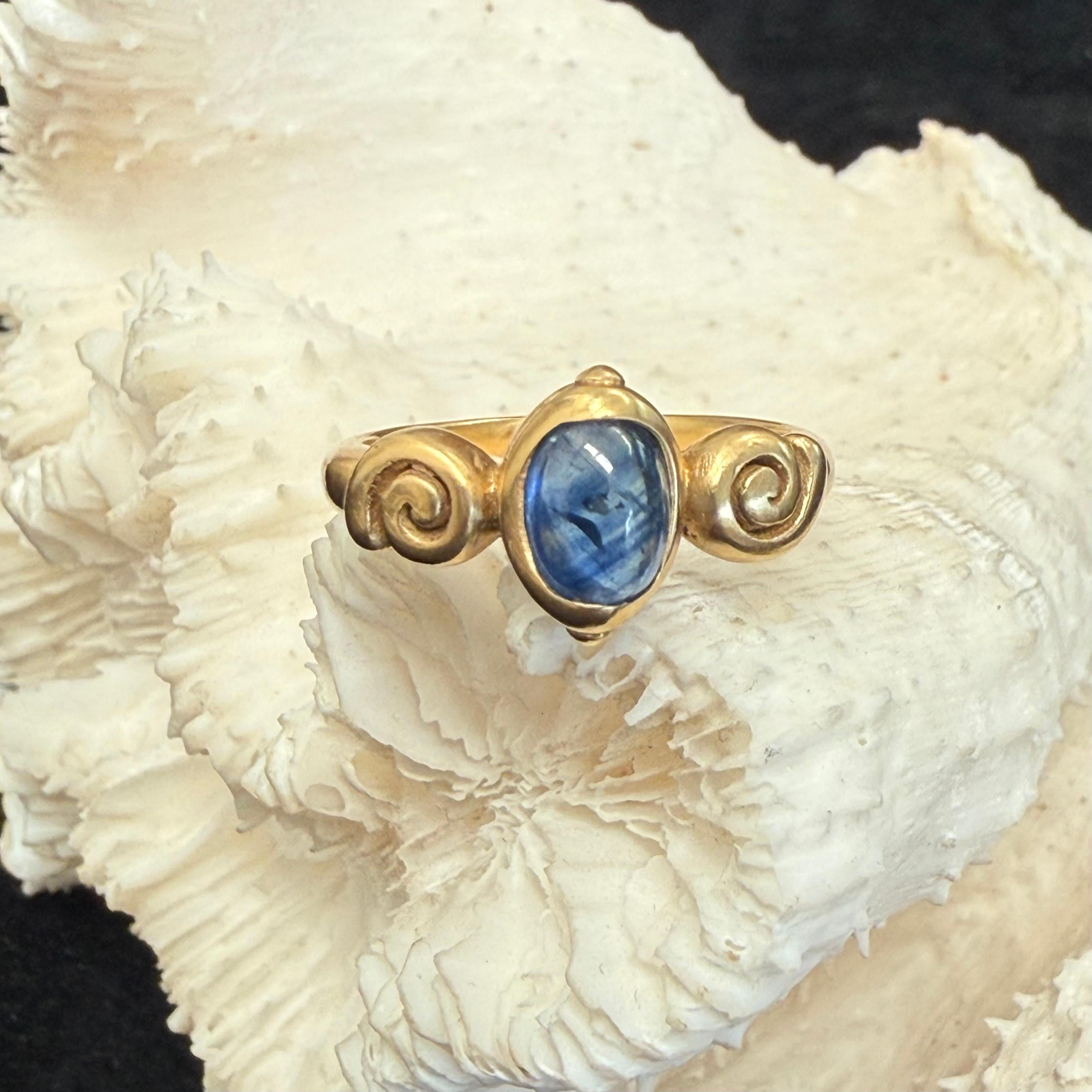 Uno zaffiro blu ovale di 5 x 7 mm è incastonato verticalmente in un castone a coppa in oro 18 carati, tra due pesanti spirali d'oro che lo circondano. Il tutto su un sostanzioso gambo con finitura opaca, attualmente di misura 6.5. Questo anello può