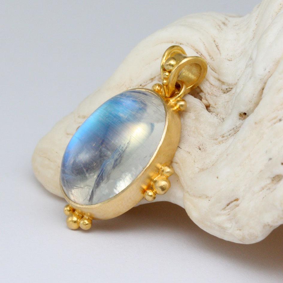 A luminous and substantial 14 x 18 mm rainbow moonstone cabochon is held vertically in an ancient-inspired 