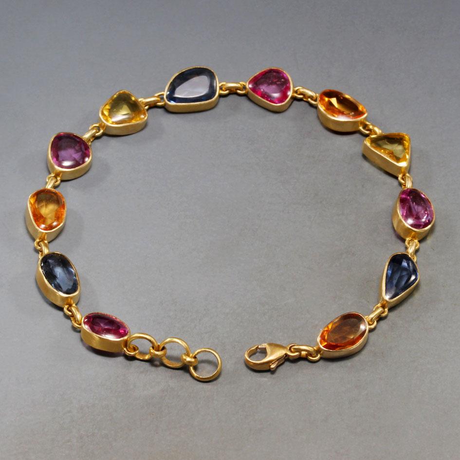 Ein lebhaftes Sortiment gemischter, ca. 6 x 8 mm großer, facettierter Saphire in Blau-, Rosa-, Gelb- und Orangetönen ist in schlichte, matte 18-karätige Goldfassungen gefasst, um dieses lebendige und phantasievolle Schmuckstück für Ihr Handgelenk zu
