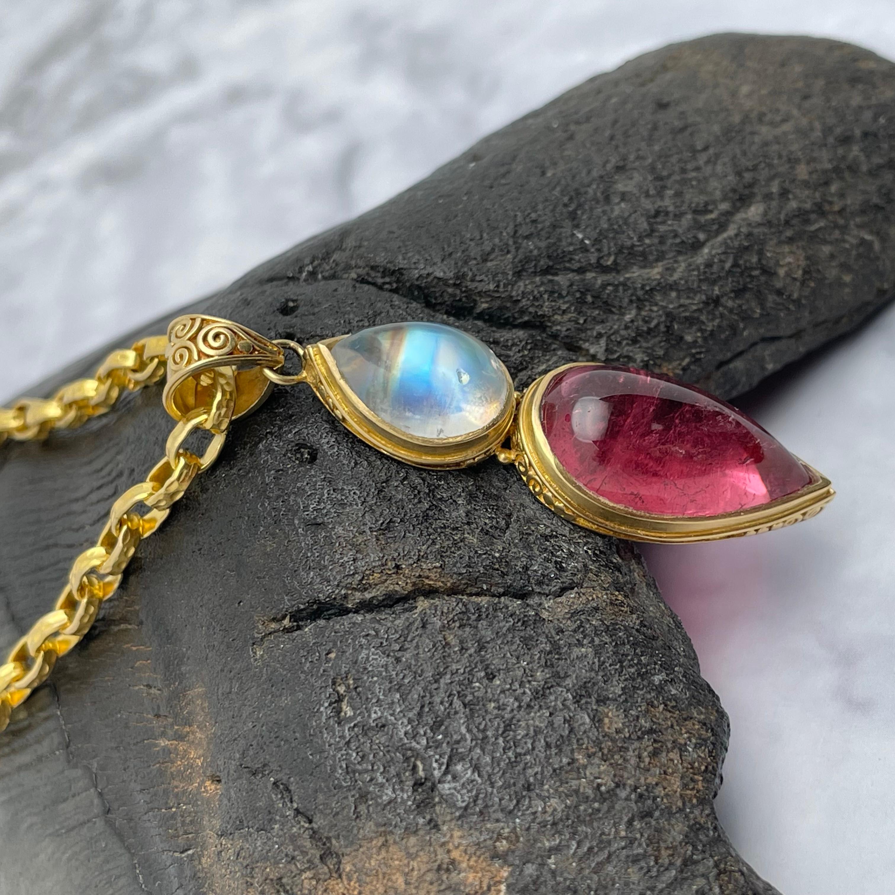 Due cabochon opposti a forma di pera di 10 x 21 mm di tormalina rosa e 9 x 13 mm di pietra di luna arcobaleno sono incastonati in castoni a spirale realizzati a mano in 18 carati sotto un'ampia cauzione a spirale in questo elegante design.  Adoriamo