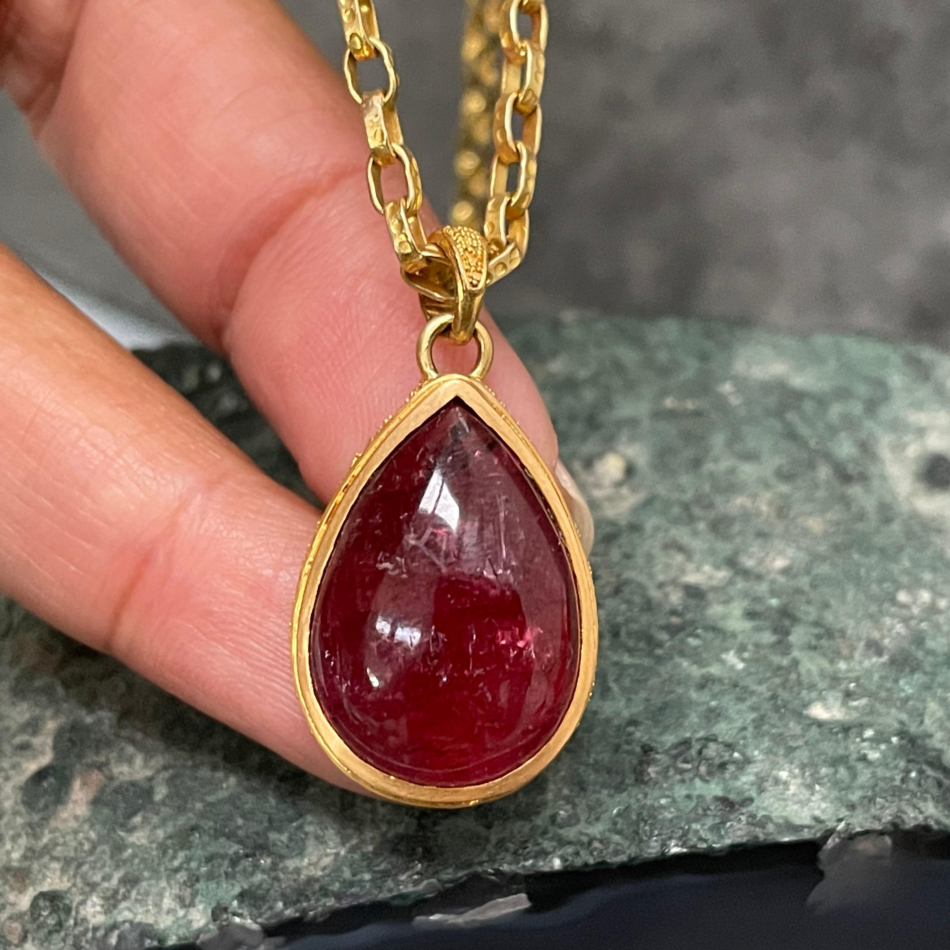 A substantial deep reddish-pink 13 x1 9 mm pear shaped tourmaline cabochon is held in a complementary 22K gold setting with fine 