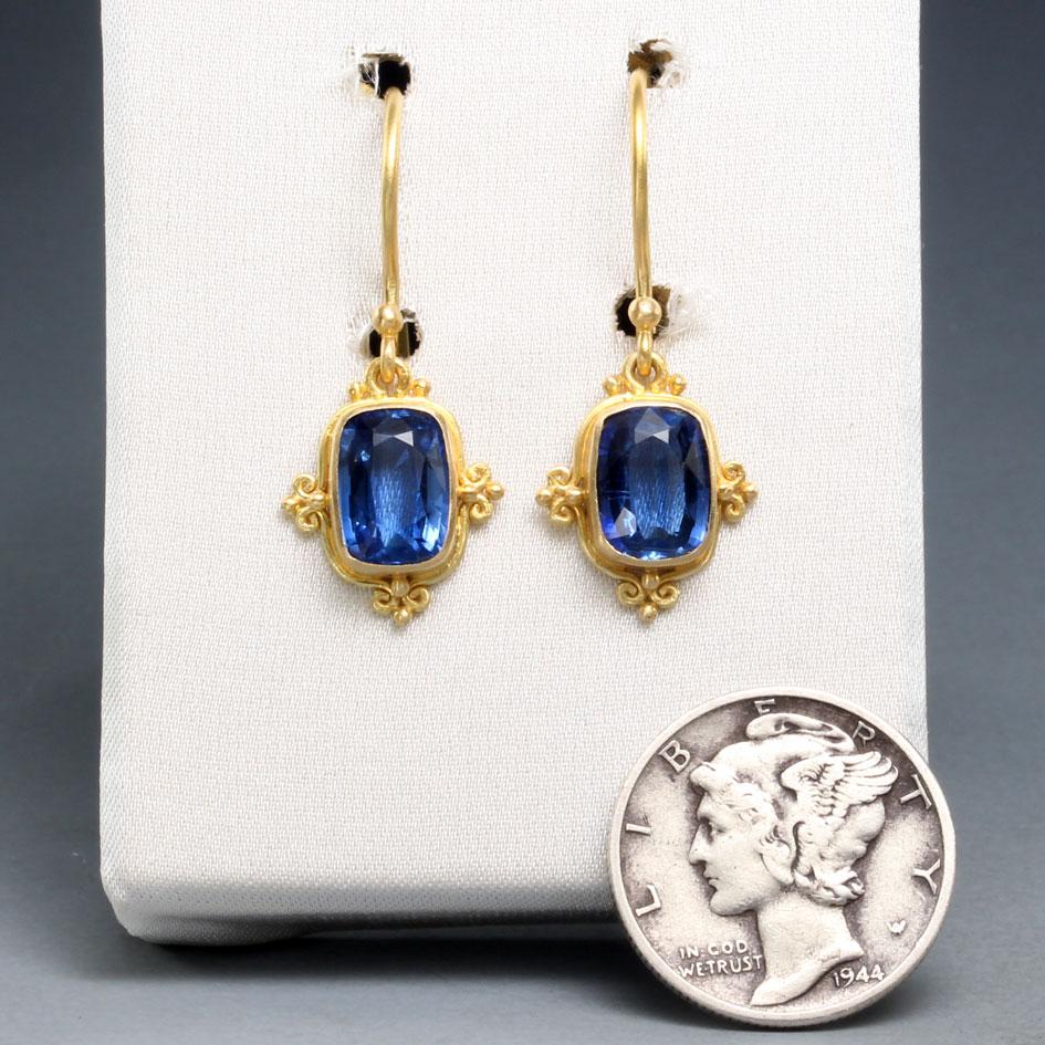 Two brilliant blue 6 x 8 mm slightly cushion shaped faceted Kyanites are set in matte-finish 18K gold bezels and surrounded by intricate 
