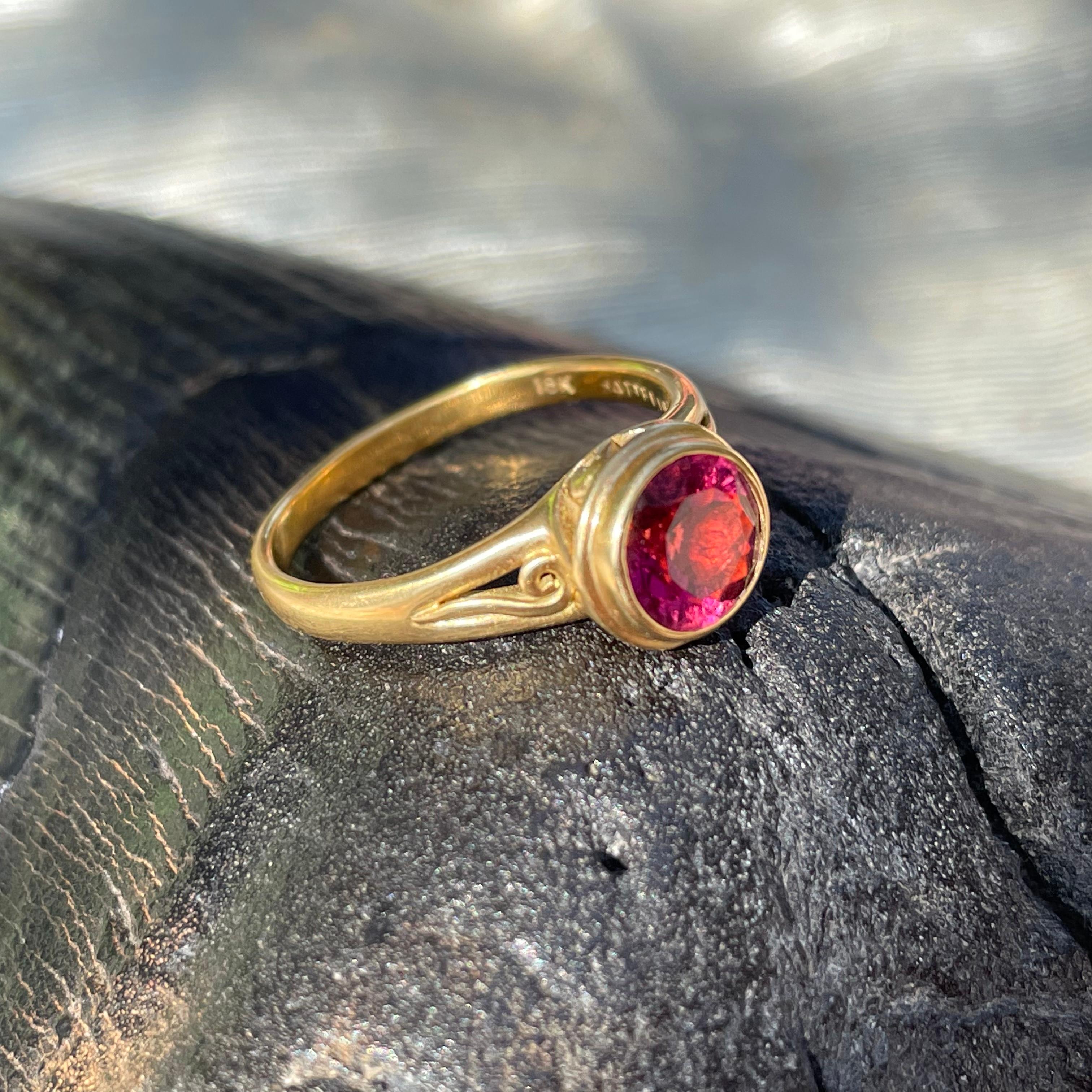 A bright pink, 7 mm round faceted tourmaline rests in a double bezel setting atop a matte-finish split shank design with a delicate spiral motif inside. This ring is currently sized 7.5. It is easily resizable.  ...Elegantly simple beauty.  