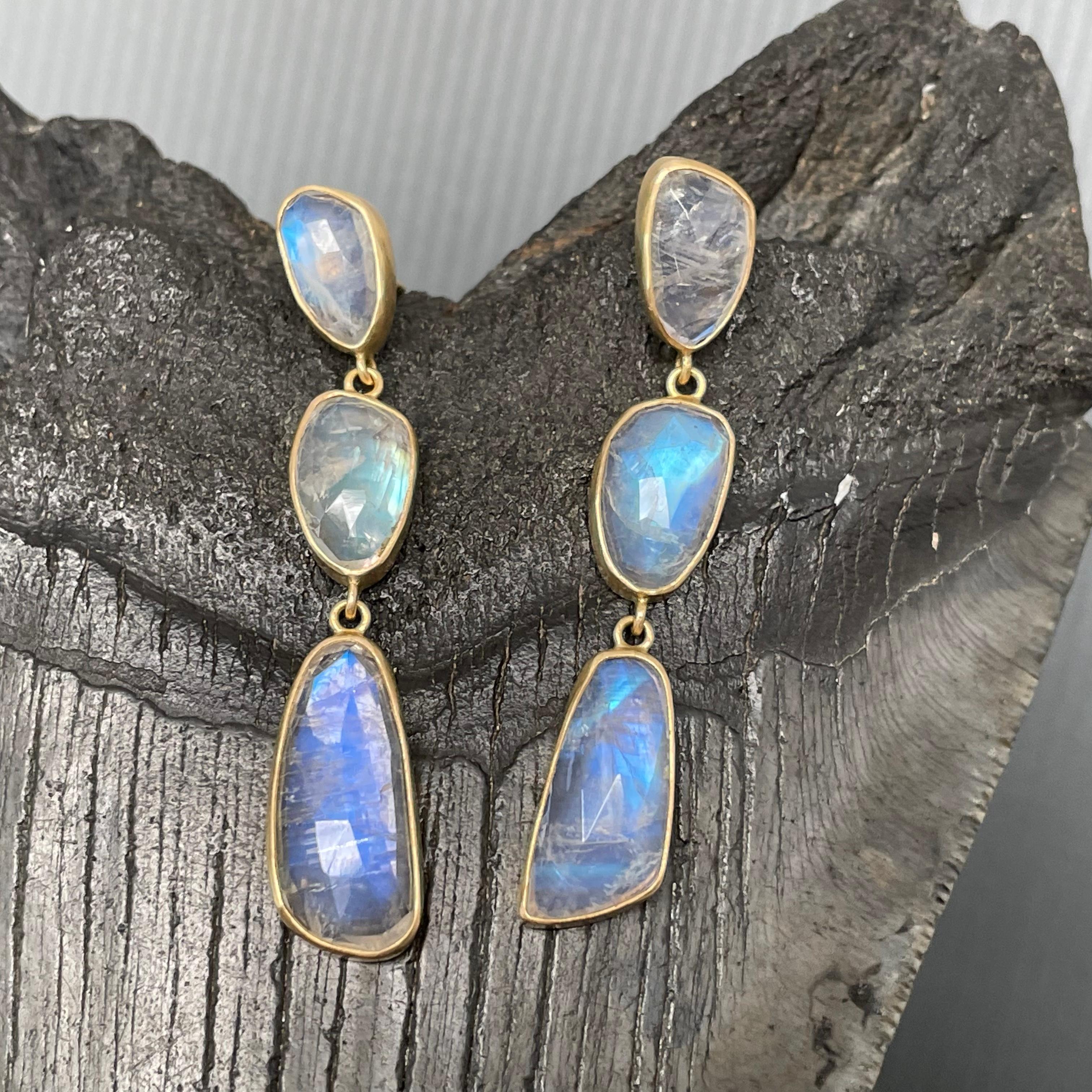 Three irregular rose-cut approximately 7 x 11 mm to 8 x 16 mm shimmering  rainbow moonstones are set in simple matte-finish 18K bezels and dangle below posts on comfortable silicone ear nuts in this design. The organic shapes draw the eye. Wow!