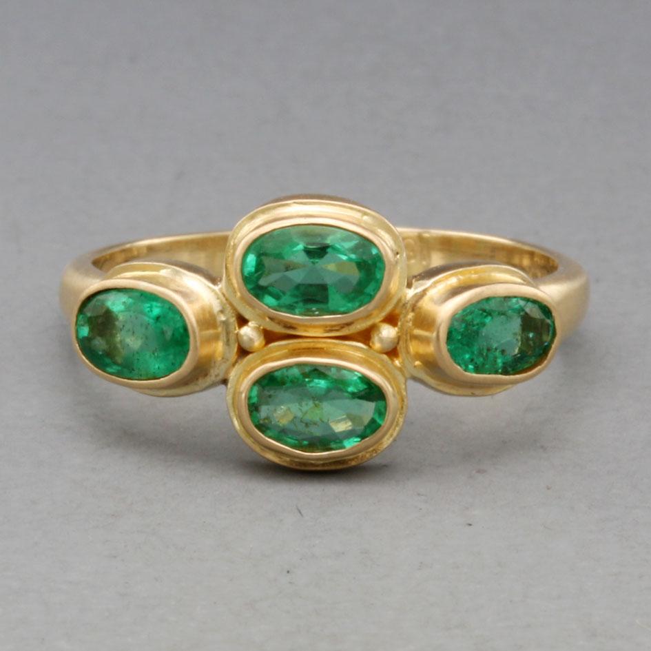Four 3 x 5 mm oval faceted Brazilian emeralds are stacked and arranged horizontally surrounded by handmade double bezel accents on a simple matte-finish 18K shank.  A pleasing look across the finger with the contrasting bright greens and gold. This