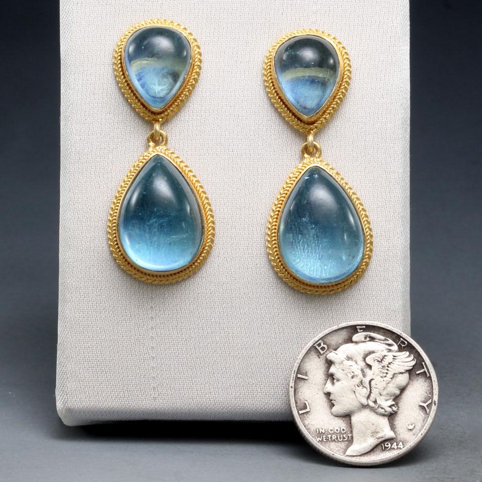 Luscious blue opposing pear shaped cabochon aquamarines of 8 x 10 mm and 10 x 14 mm are surrounded by delicate 