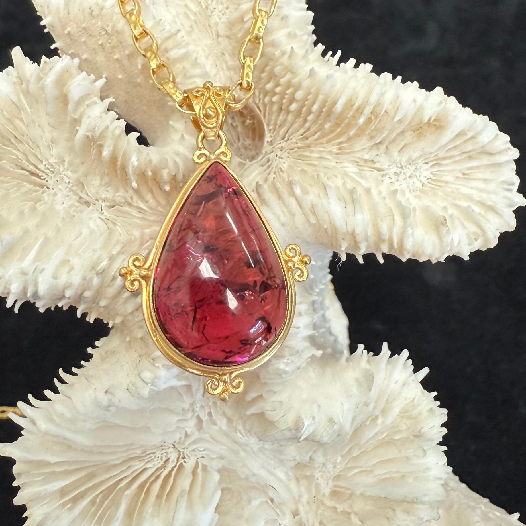 Ein lebendiger, rötlicher, 15 x 23 mm großer, birnenförmiger Mosambik-Rosa-Turmalin-Cabochon wird in einer matten 18-karätigen Goldfassung mit drei 