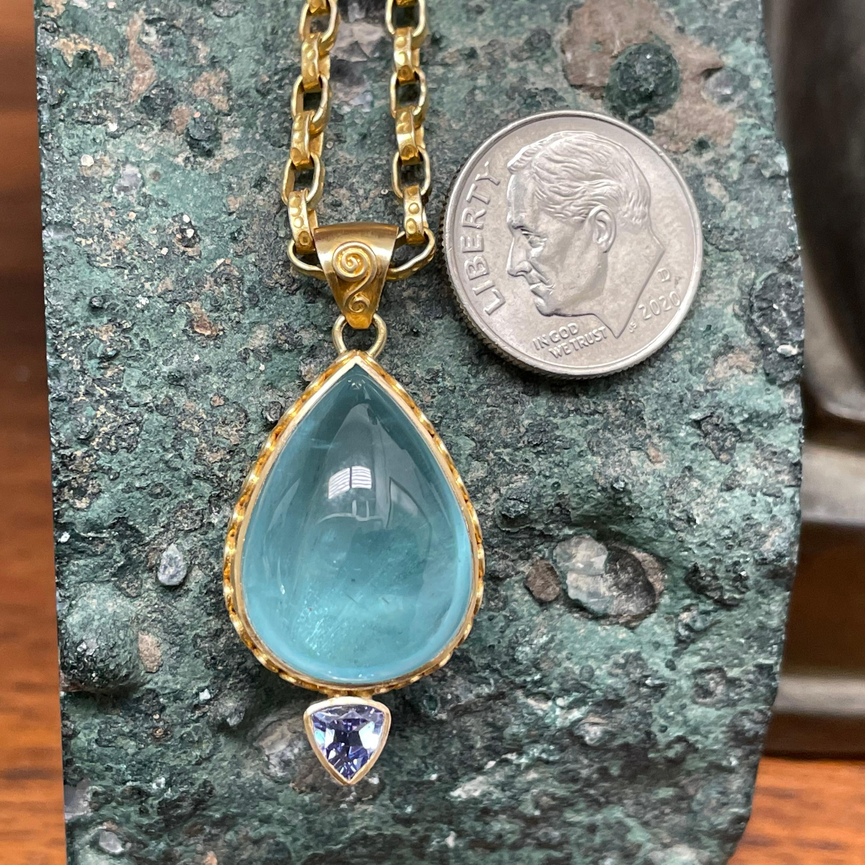 A nice blue, limpid, pear shaped 15 x 19 mm aquamarine cabochon is centered above a 5 mm trillium faceted tanzanite in this Steven Battelle ancient-inspired design.  The aquamarine cabochon is surrounded by 18K gold doubled spirals handwork on the