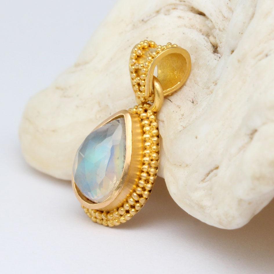 A shimmering 7 x 9 mm pear shaped faceted rainbow moonstone is surrounded by a double layer of stacked 