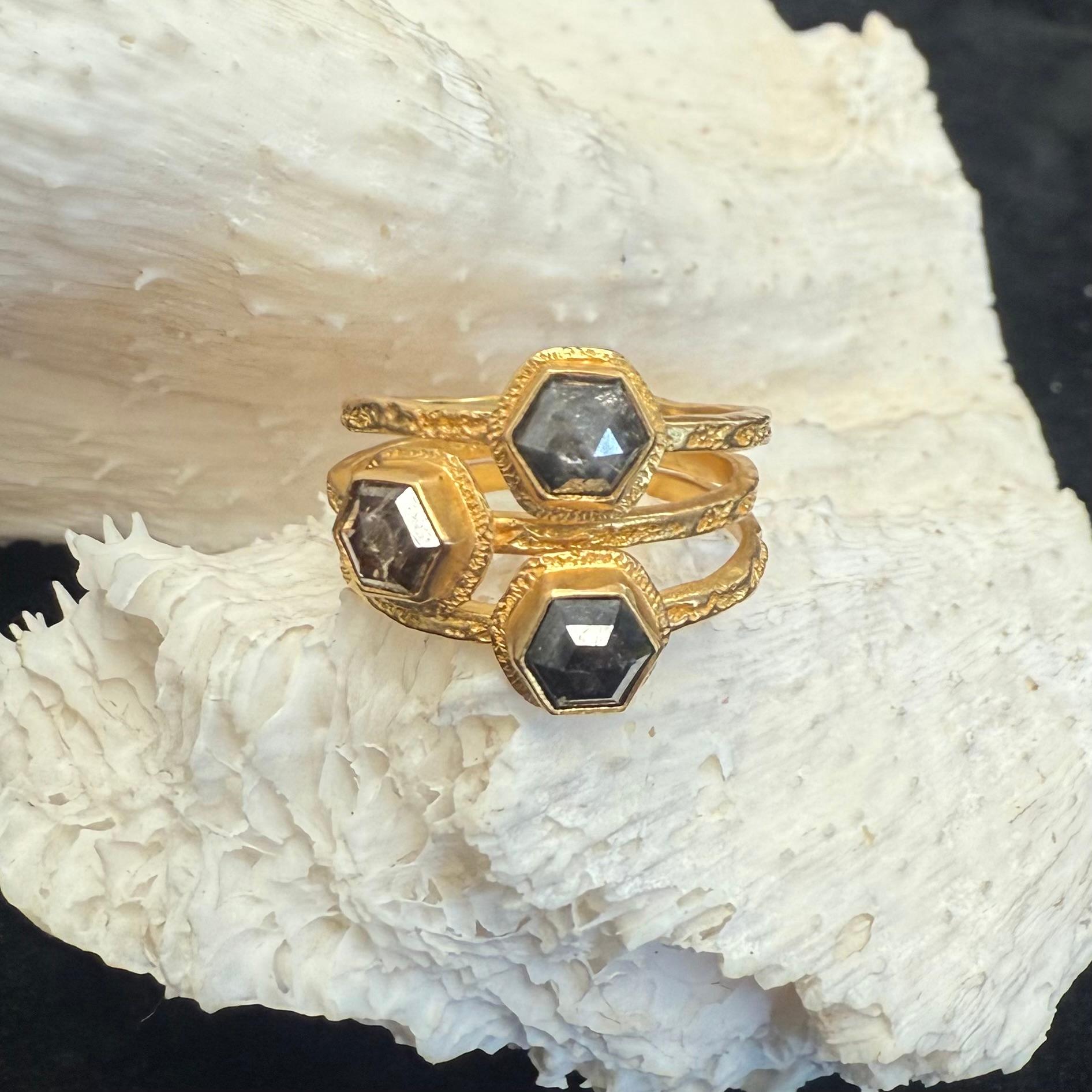 An interesting assortment of 4-5 mm hexagonal colored diamonds are set in hand-textured bezels atop squarish organic textured 18K gold bands that are attached together at the bottom.  Altogether, they create a look that is refreshing, fascinating,