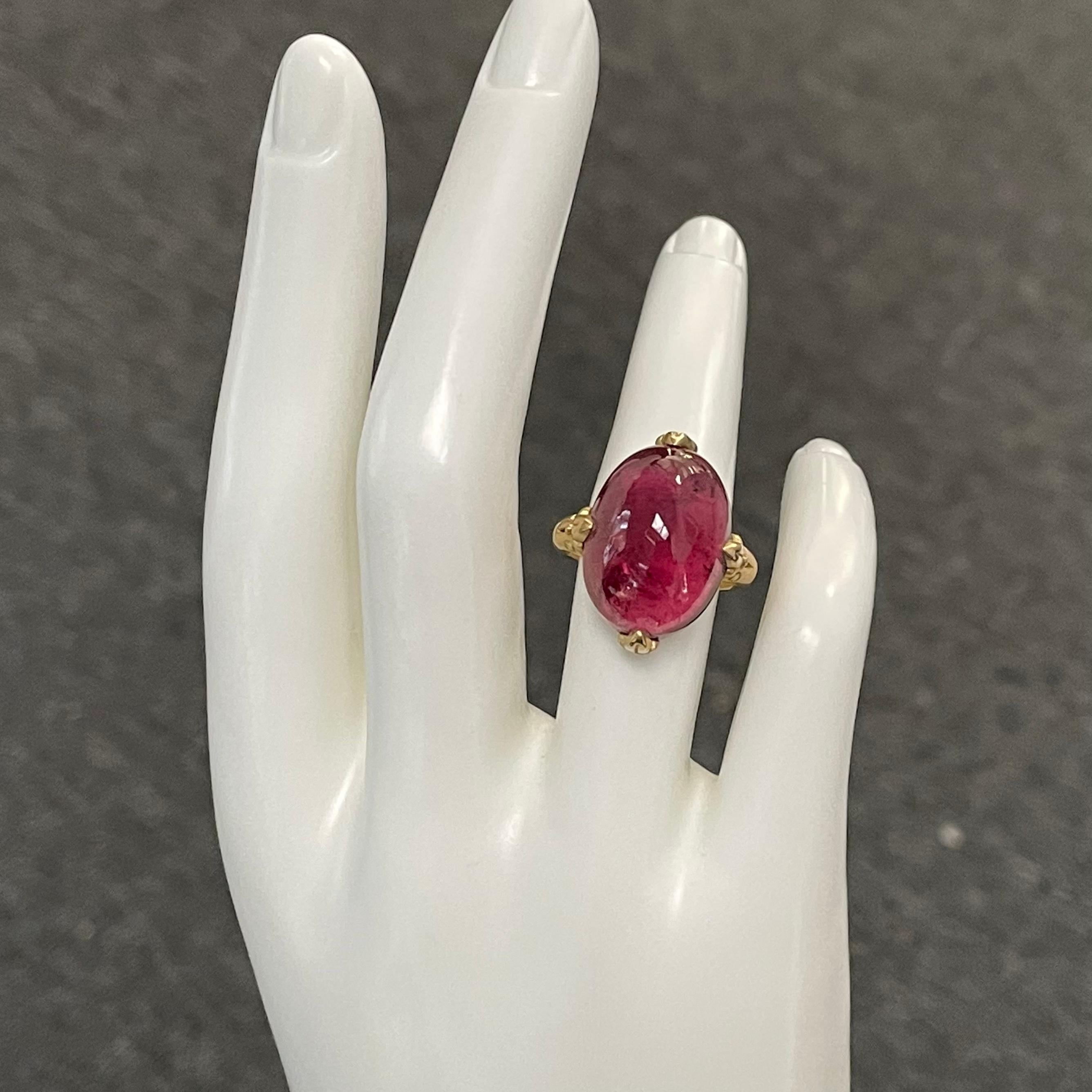 A clear 13 x 18 mm cabochon cut salmon pink tourmaline is held in 4 carved prongs in this Steven Battelle designed 18K gold setting.  This allows for lots of light interplay and a lively stone.  
A tapered matte finish shank currently sized 7