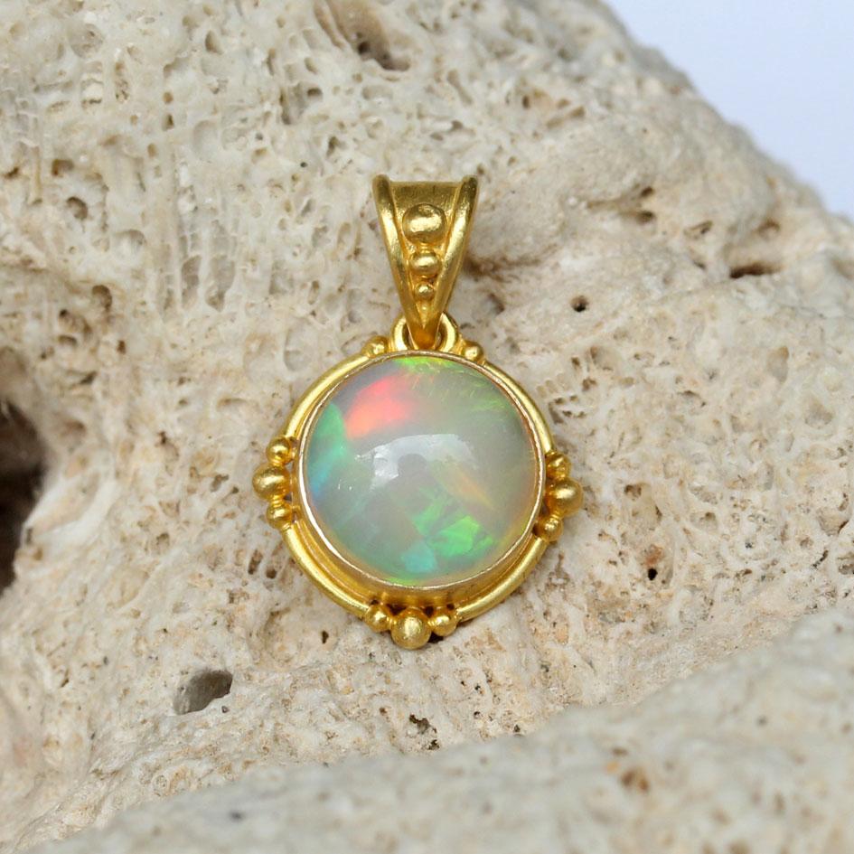 Un opale etiope rotondo di 10 mm, verde, rosso e blu, proveniente dalla famosa miniera di Welo, è incastonato in un castone di 18 carati lavorato artigianalmente e circondato da 