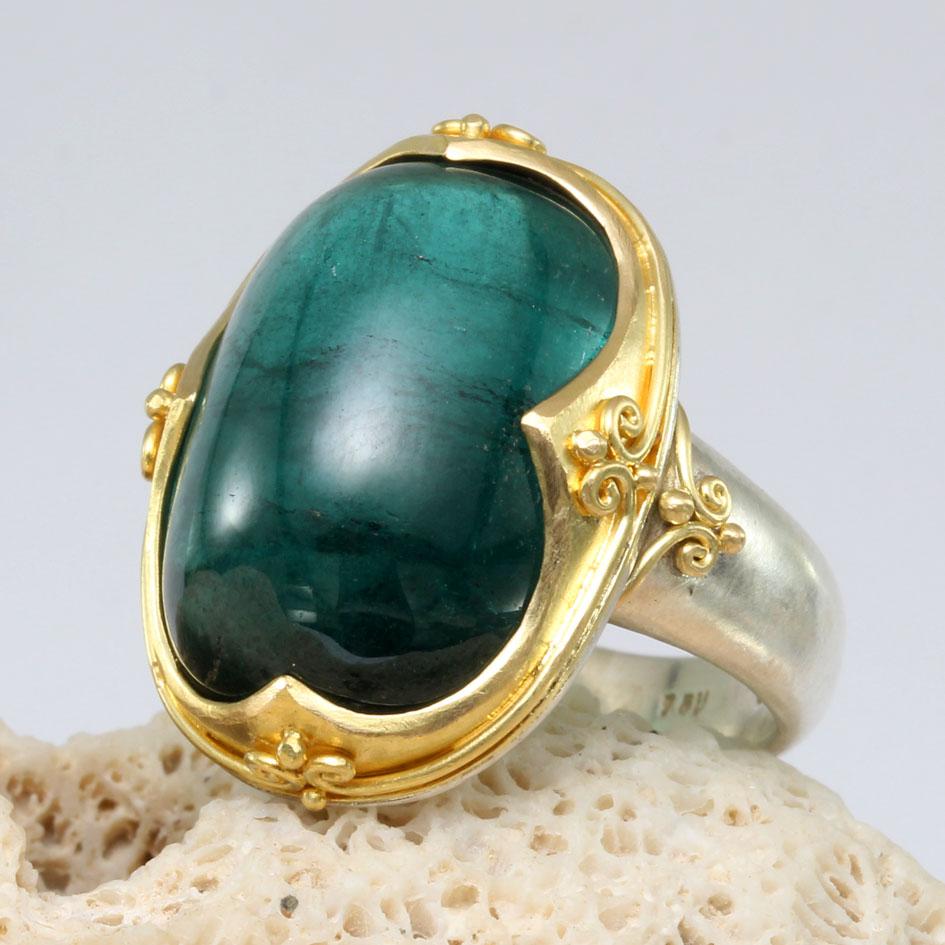 Un grande cabochon di tormalina verde Indicolite di 15 x 20 mm è incastonato verticalmente in un'incastonatura in oro 18 carati a 4 punti con filo a spirale e jawan, su un gambo in argento sterling dalla finitura opaca in questo design di