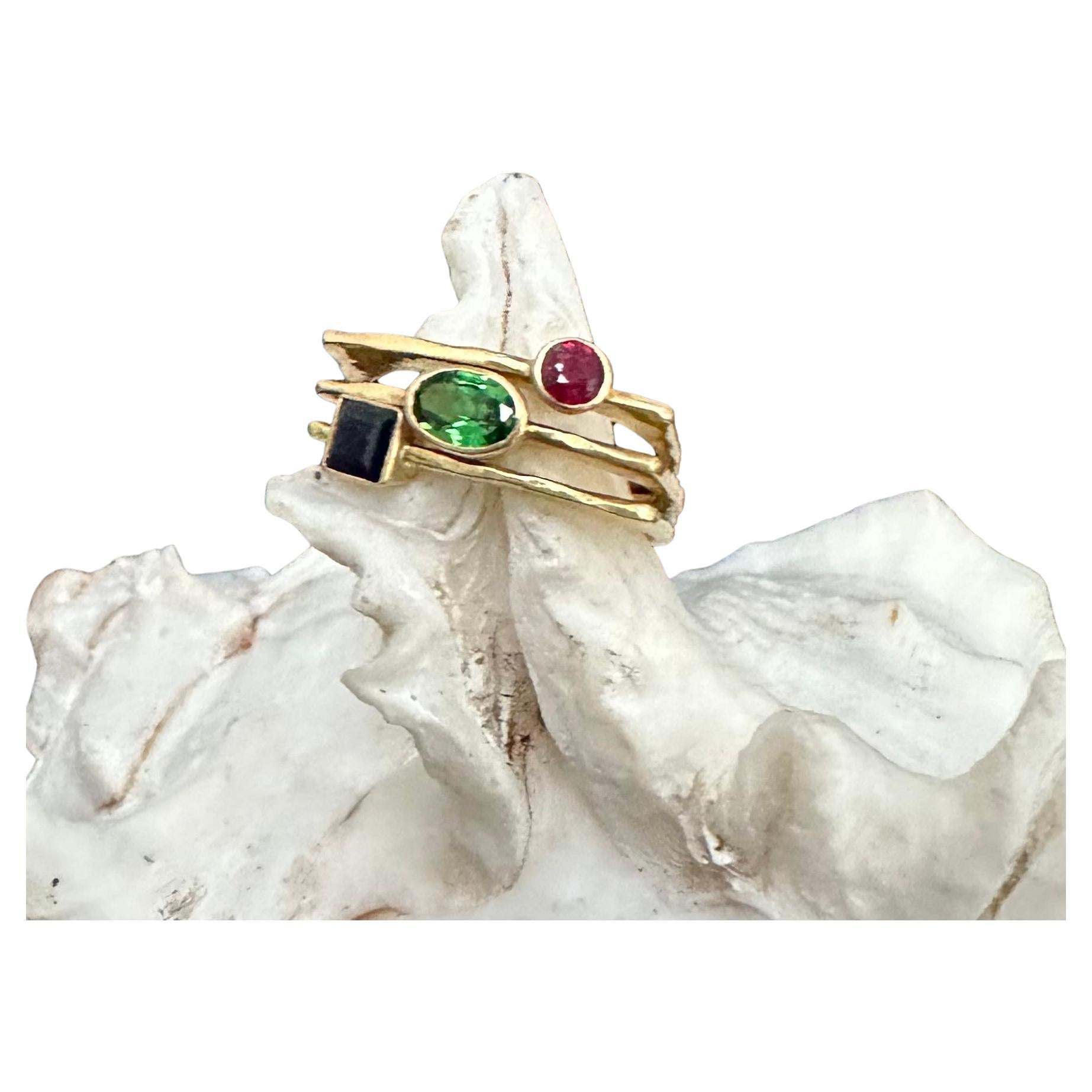 A faceted 4 x 6 mm Tsavorite, 4 mm square faceted Blue sapphire, and 3 mm round faceted Ruby align diagonally across 3 uniquely shaped hammered shanks that fit together for an interesting semi-flat organic and geometric combination look at the top,