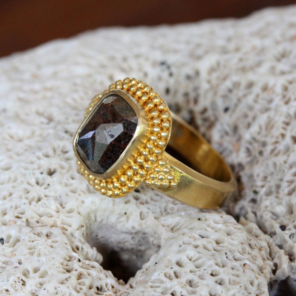 An 8 x 10 mm brown-black cushion shaped rose-cut diamond is set vertically surrounded by a double row of handset 