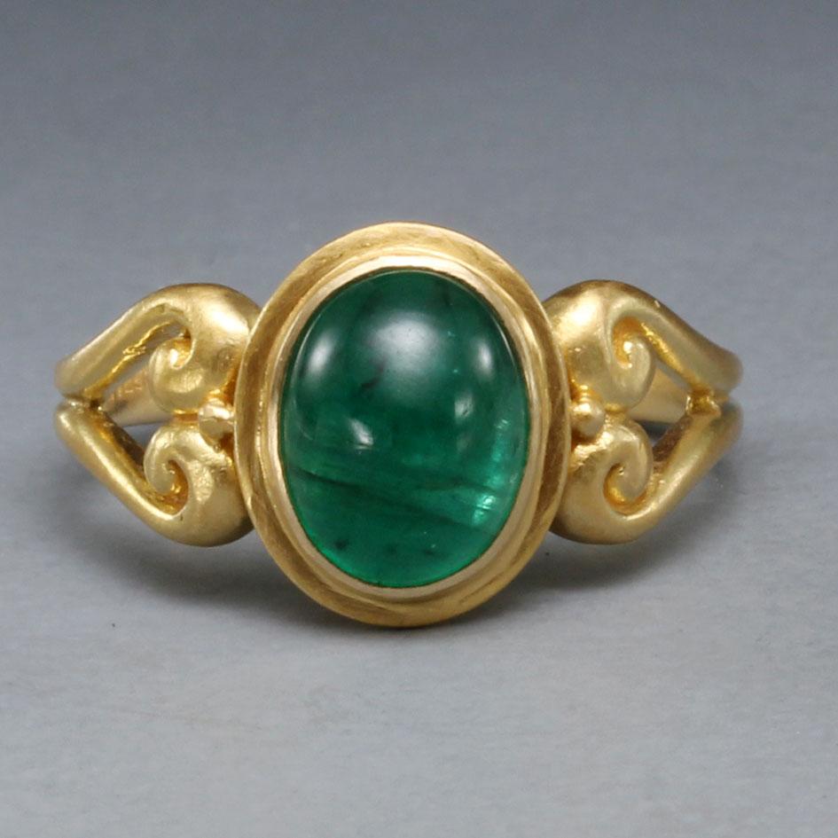 A lively deep green 7 x9 mm cabochon Zambian emerald sits vertically in an 18K embrace within luxurious thick opposing curved spirals with side attached 
