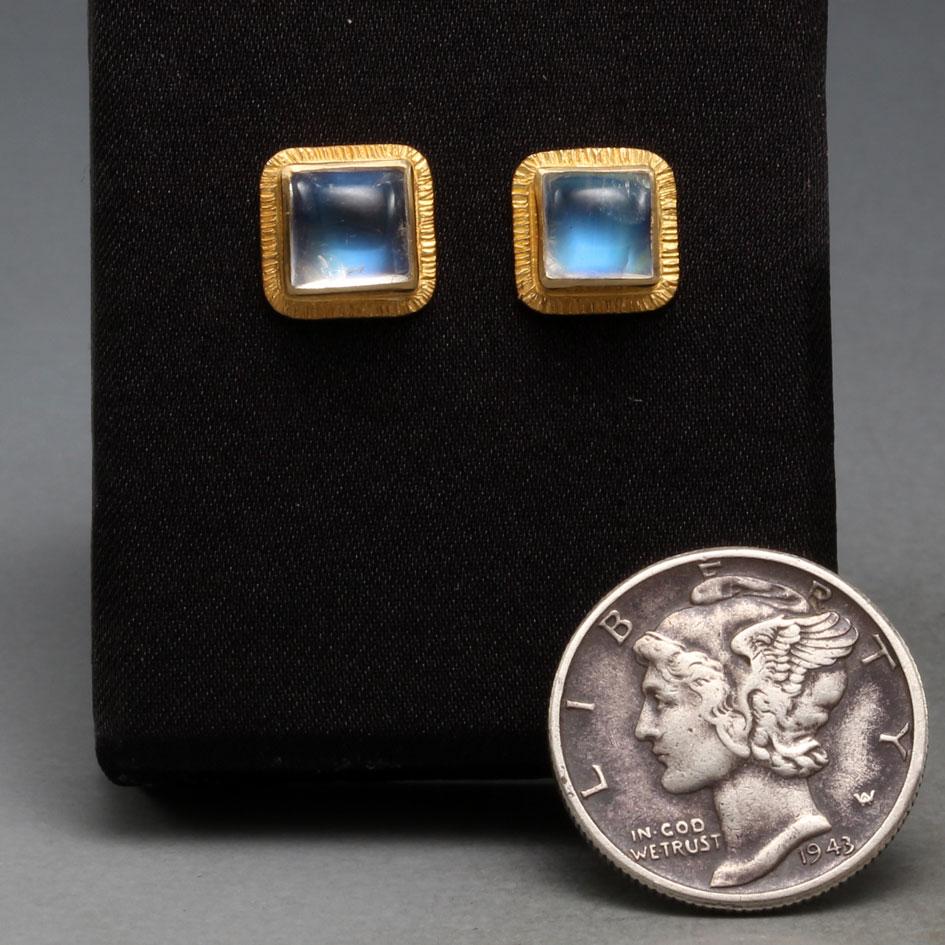 Two blue shimmering 6 mm square cabochon rainbow moonstones are surrounded by line textured 18K gold double bezels in these ultimately simple and classic posts.  The contrast between the blue sheen and rich gold texture is super nice.  Everyday
