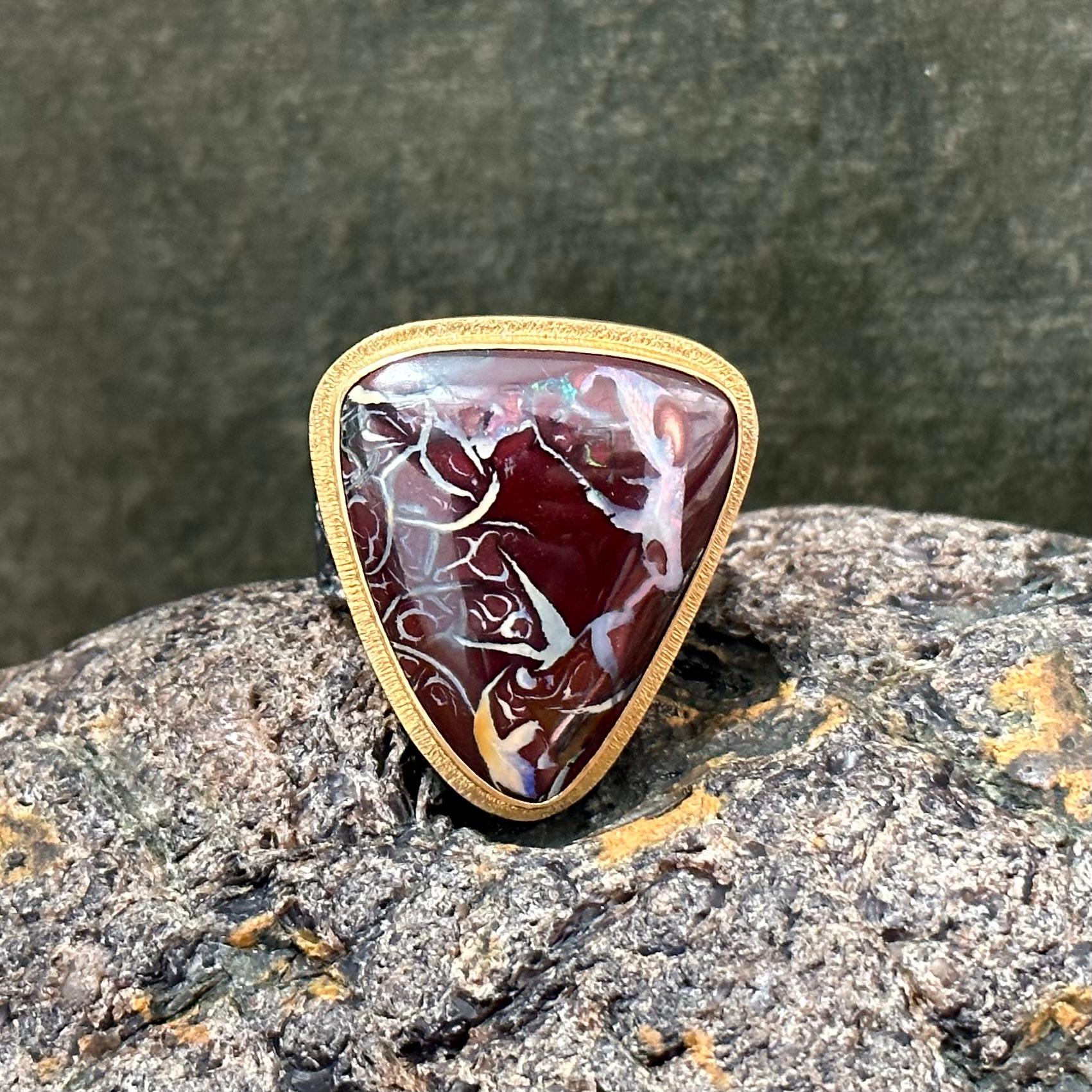 A fascinatingly unique 21 x 25 mm trillium cabochon of Australian Koroit Boulder Opal is highlighted with an 18K gold bezel surrounded by a line textured double bezel atop a comfortable flattish organically textured contrasting dark oxidized
