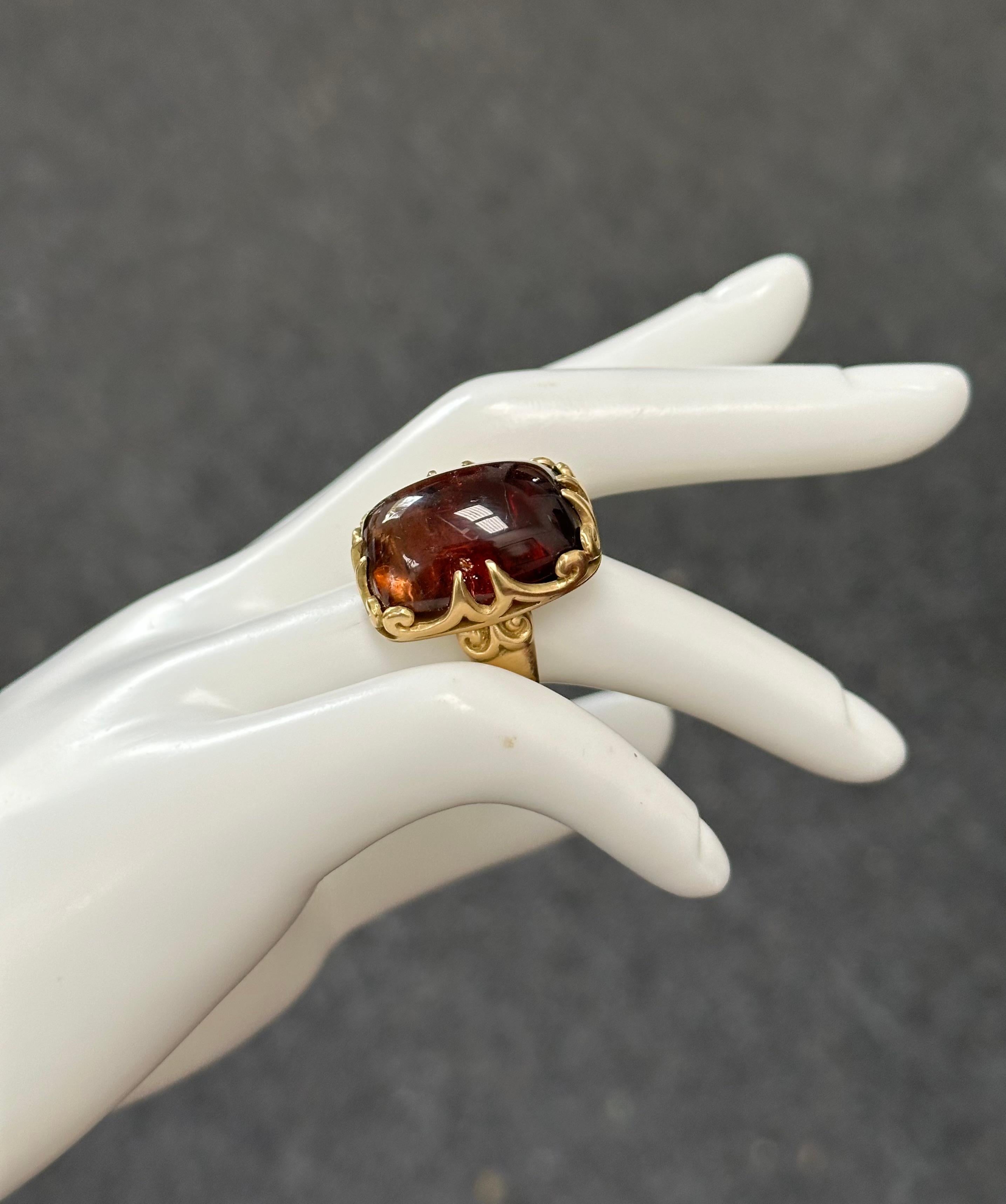 Un cabochon de tourmaline melon d'eau de 14 x 19 mm de forme coussin, présentant principalement des nuances de rouge et d'orange, est serti verticalement dans une intéressante monture en 