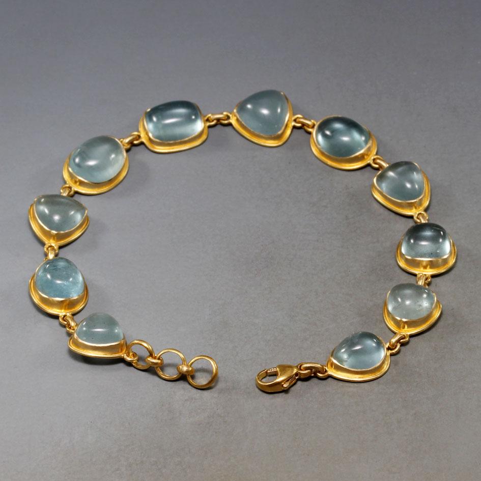 Eleven irregular cabochons of limpid light blue-green aquamarine are set in cupped handmade 18K gold bezels surrounded a double bezel accents in this design.  The stones are approximately 7 x 9 mm in size and vary among oval, round, trillium, and