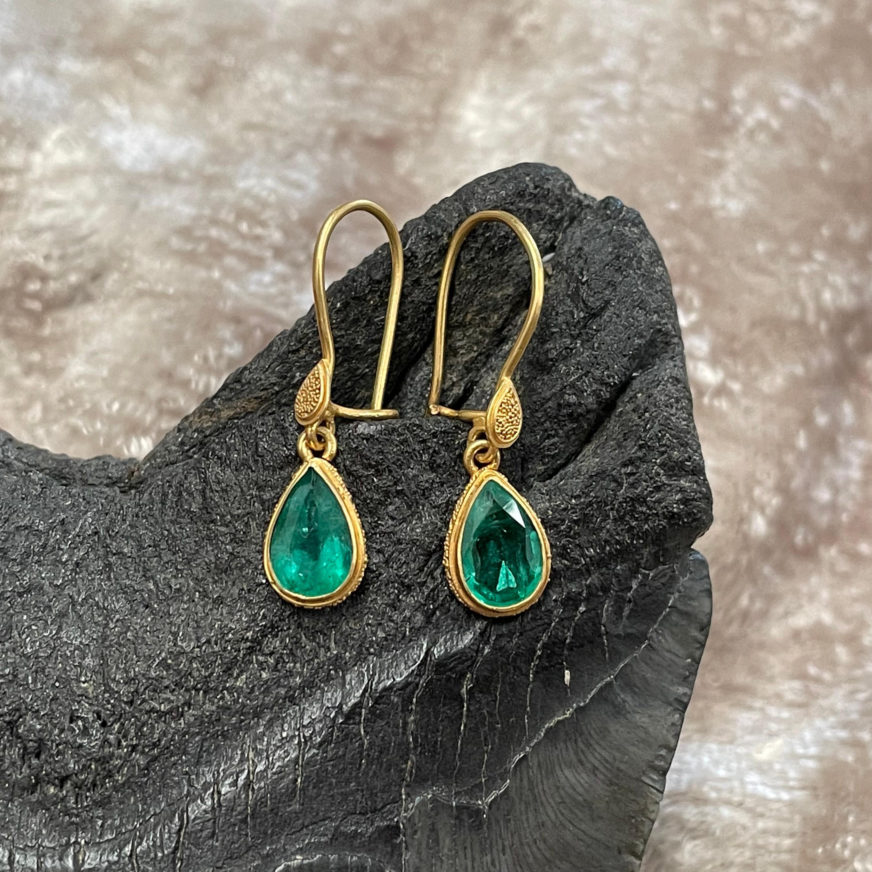 A pair of lively 6x9 mm pear shaped faceted Zambian emeralds are gently suspended in a 22K settings with fine 