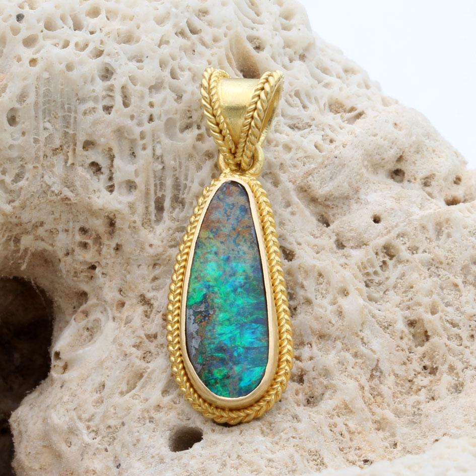 Ein feuriger, grün blinkender, unregelmäßig geschliffener 6 x 16 mm großer australischer Boulder-Opal aus den Opalfeldern in der Nähe von Quilpie, Queensland, ist in eine handwerklich gefertigte, mattierte 18-karätige Goldlünette eingefasst, die von