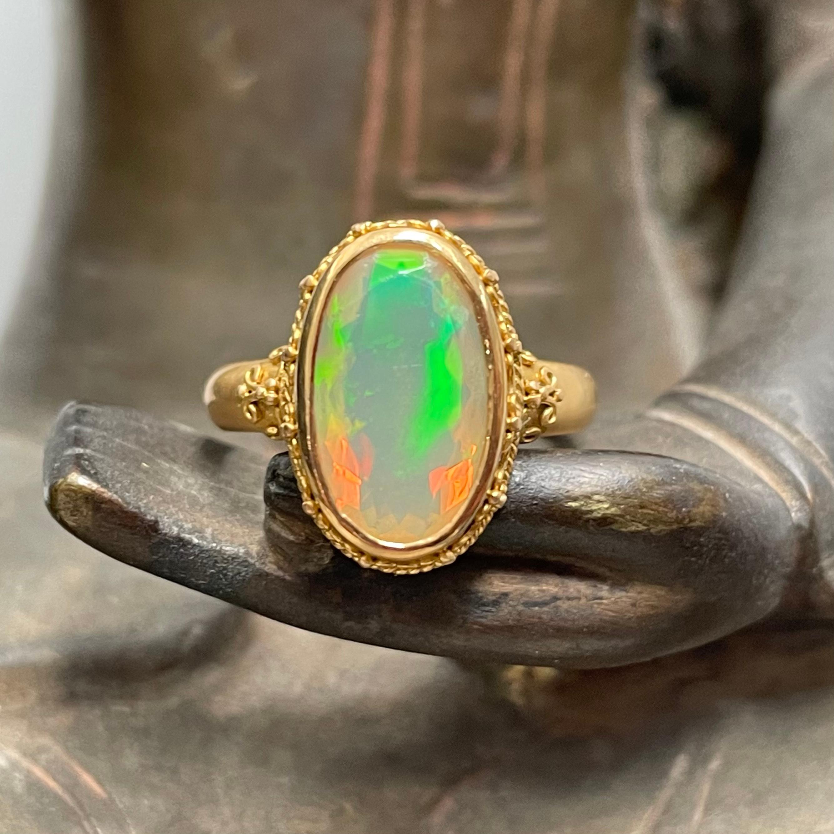 A long 8 x 13 mm oval faceted Ethiopian opal with flashes of orange and green is held by a hand applied wire and 