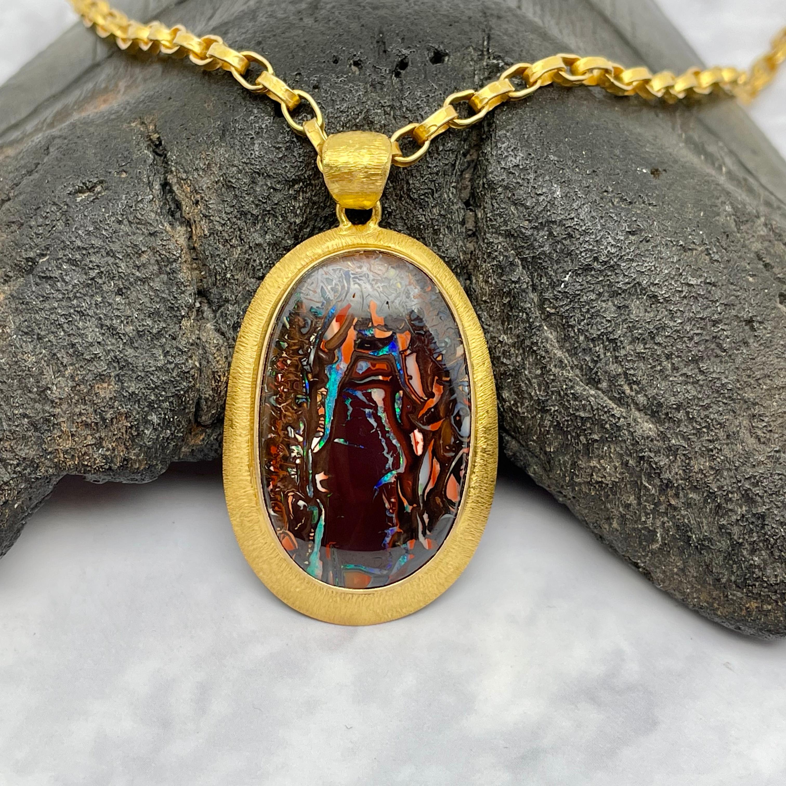 A nice 18 x 29 mm oval harlequin Koroit boulder opal with nearly every rainbow color displayed is highlighted in a double line texture handmade 18K gold setting with similar wide bail.  Koroit opal comes from an opal mining area in Paroo Shire in