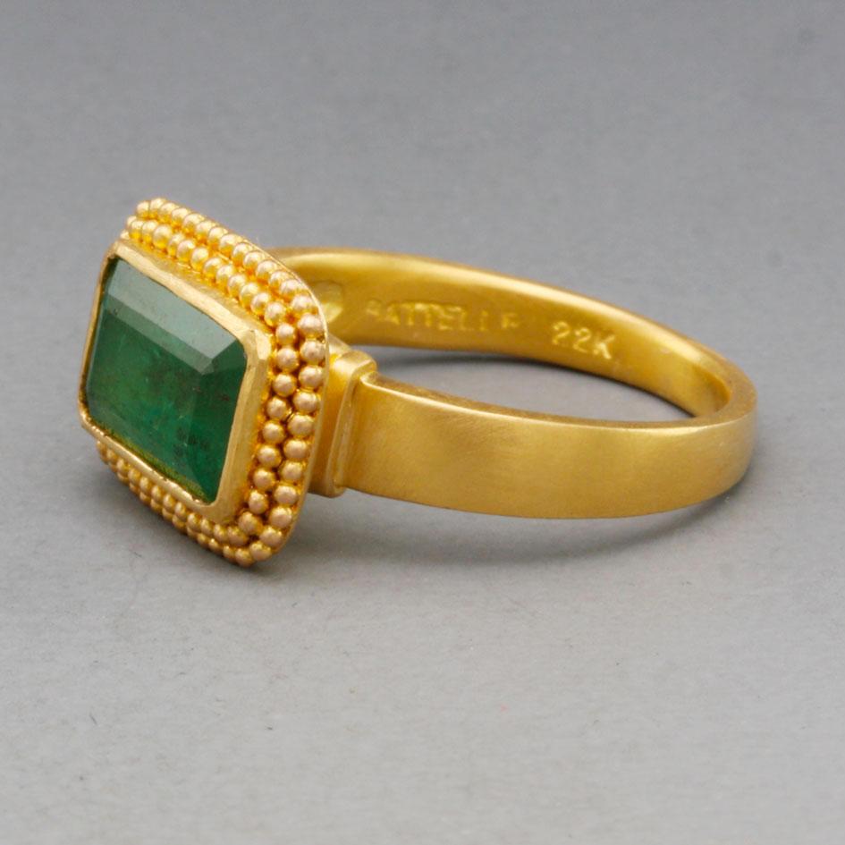 A 2.8 carat 6 x 11 mm octagonal cut Zambian emerald is mounted horizontally, surrounded by a double row of  