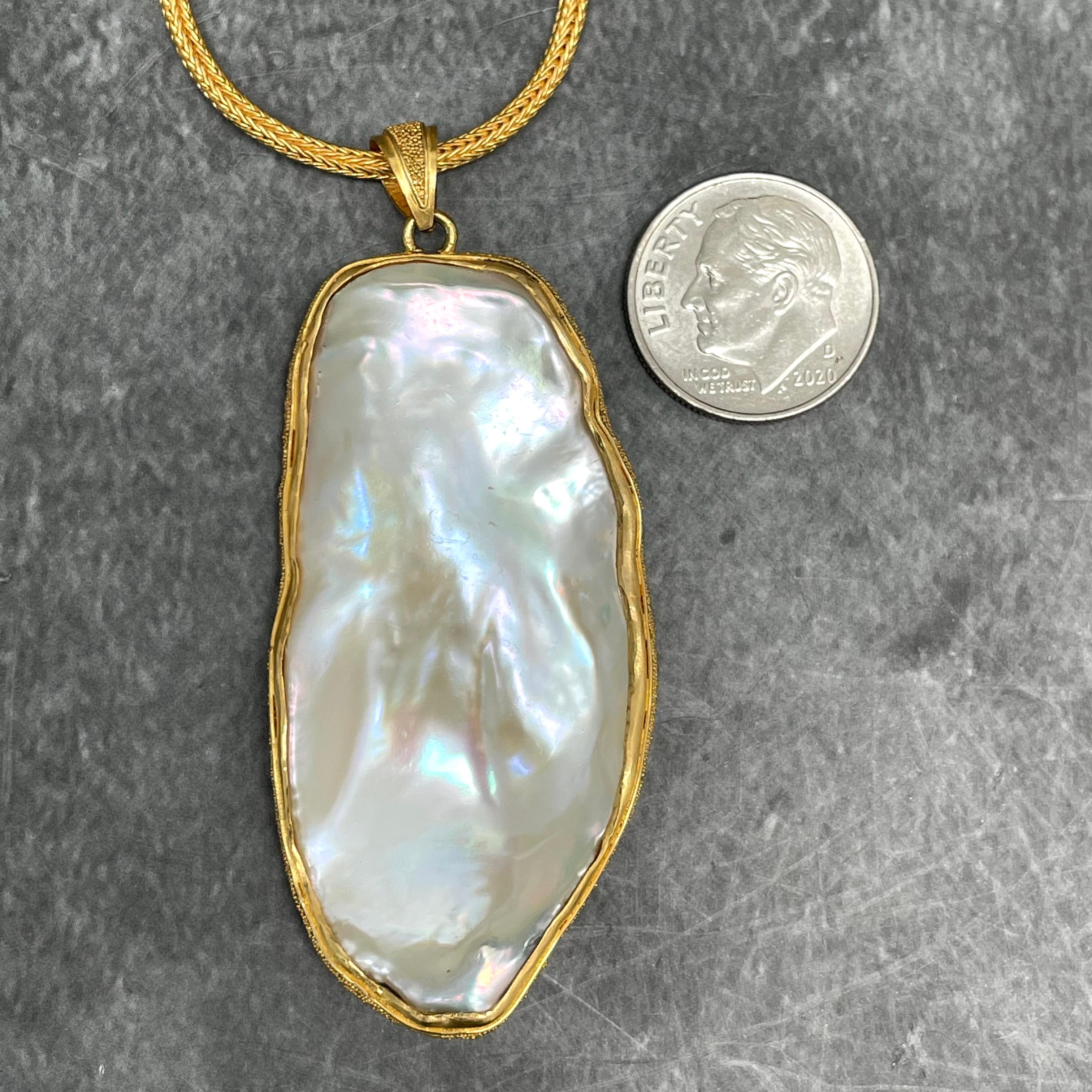 A lustrous, approximately 25 x 50 mm flattish white freshwater pearl is held with rich 22K gold accented with delicate 
