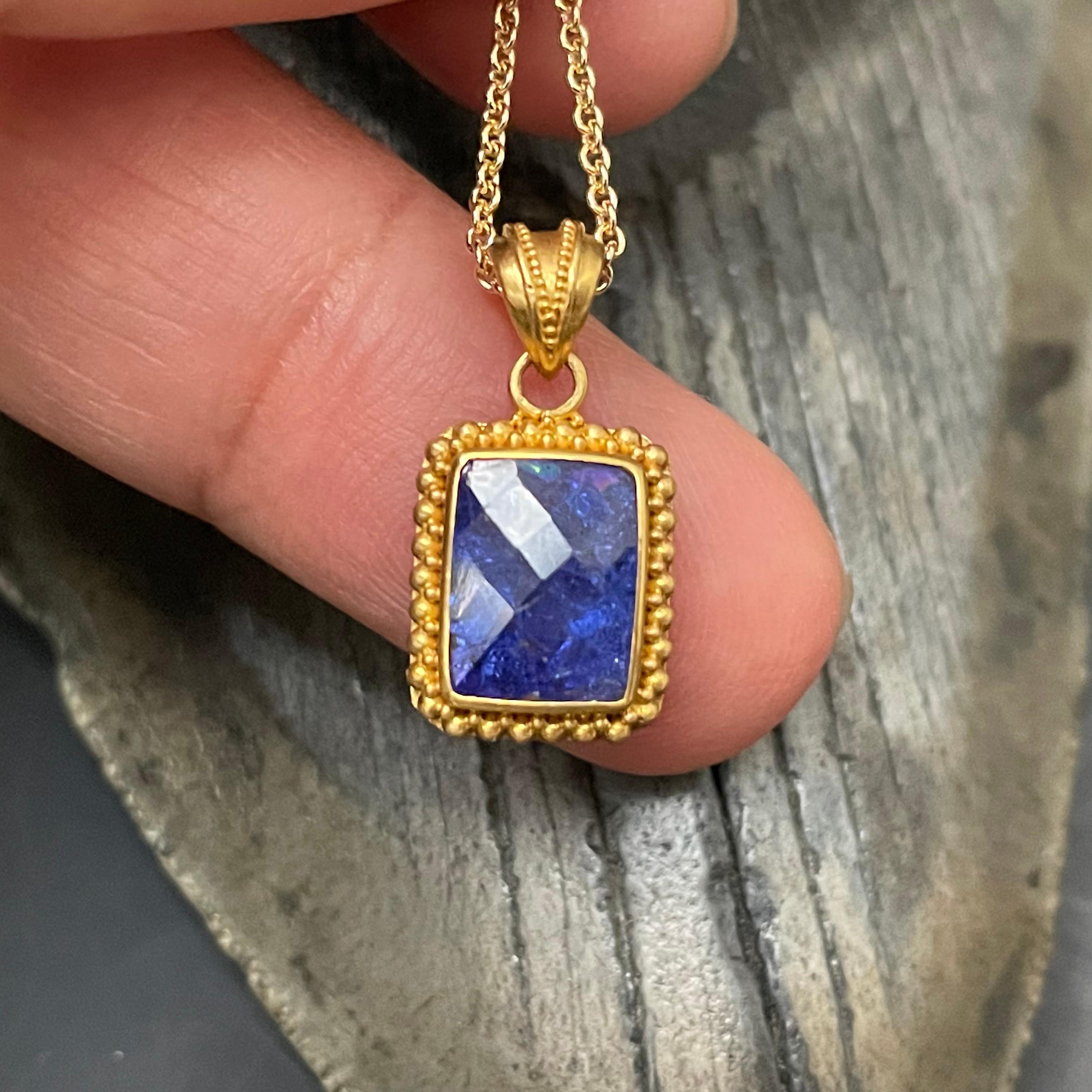 I lively deep blue/purple 7 x 9 mm rectangular rose cut tanzanite is highlighted within a 22K granulated 
