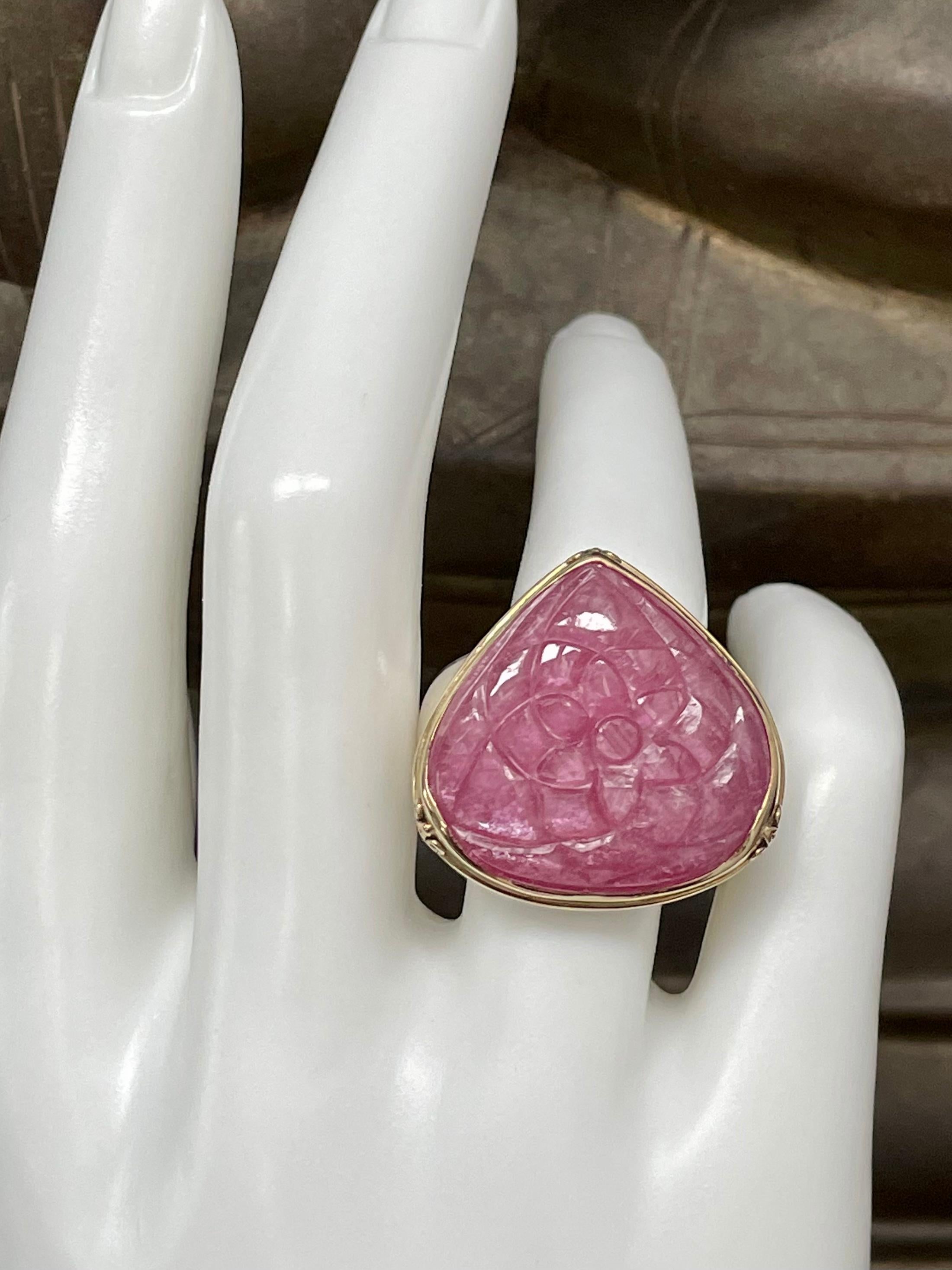 A large, 22 mm wide pear shaped florally carved pink ruby cabochon is held in an 18K gold bezel with 3 small corner spiral ornaments atop a wide sterling silver shank in this statement design. 
A lot of ruby and ring for an affordable price! 