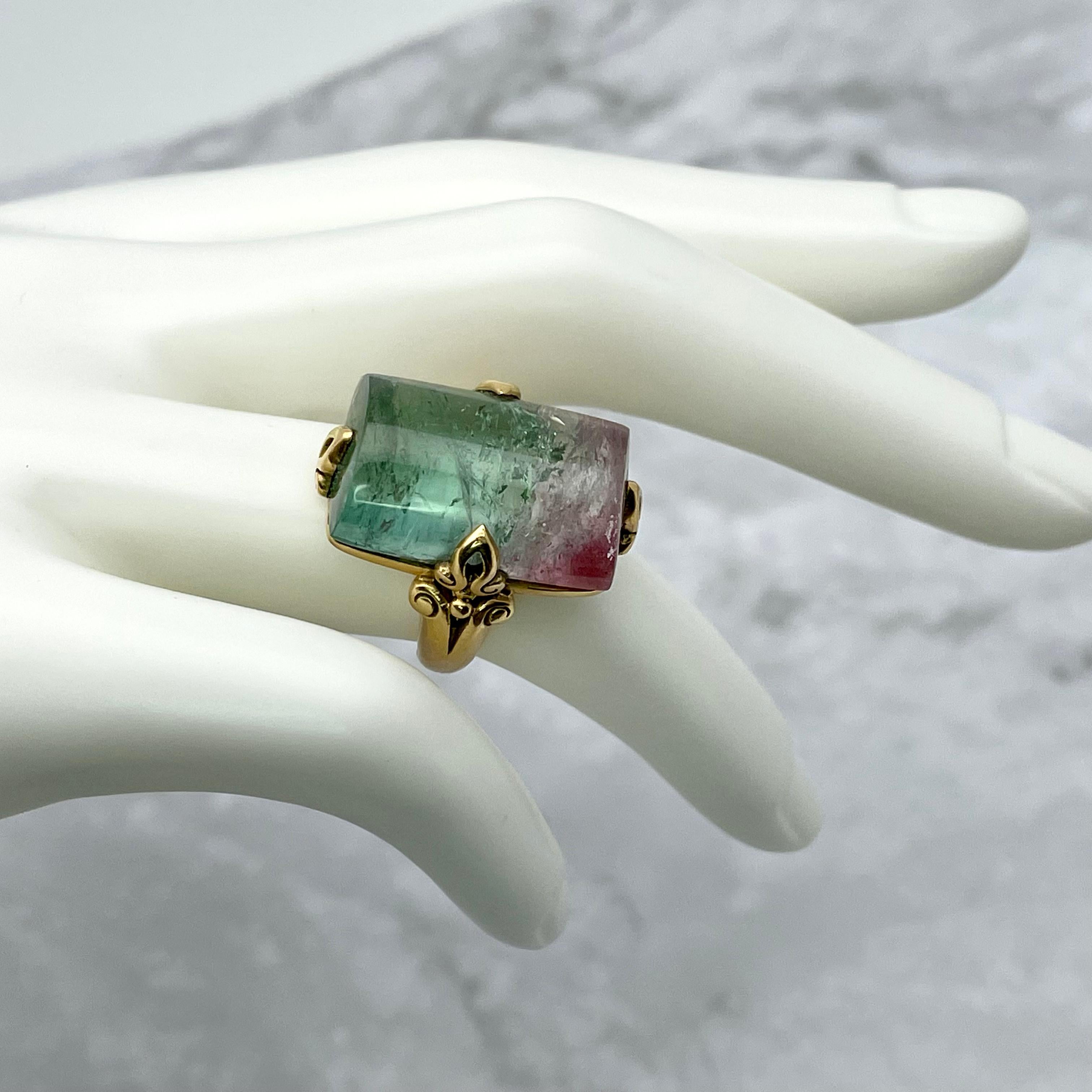 A vibrant half cylinder of cabochon watermelon tourmaline crystal is held by four carved 18K prongs atop an ancient-inspired double spiral matte finish gold shank.  This stone has beautiful shades of light green to pink with lots of internal