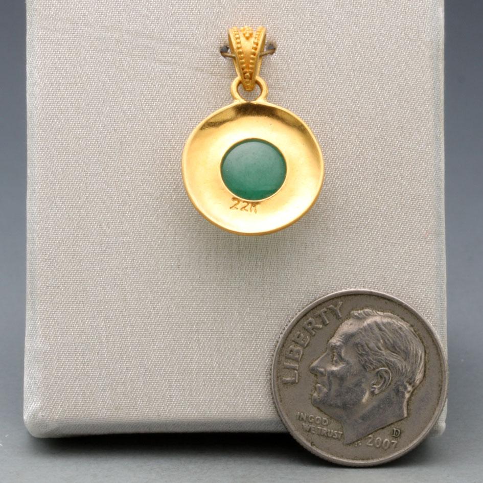 A round 9 mm cabochon Zambian emerald is set in a beautifully crafted classic handmade granulated high-karat gold setting.  The clear greens of the emerald contrast against the rich yellows of the geometric 